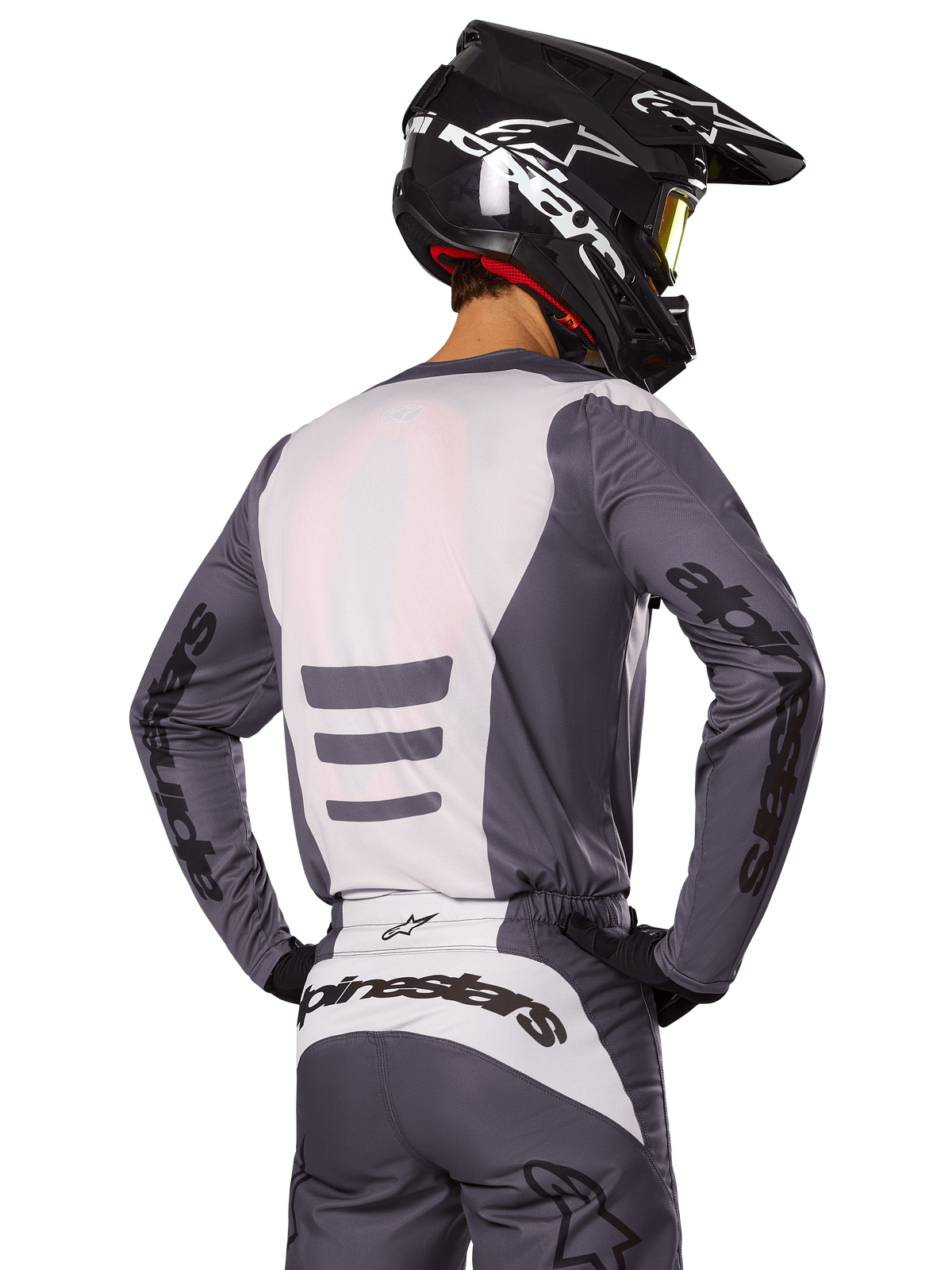 Pilote de motocross de dos portant l'ensemble d'équipement Alpinestars Fluid Haul 2025, maillot et pantalon gris et blanc, casque noir avec graphismes blancs, lunettes jaunes, tenue de course de motocross coordonnée