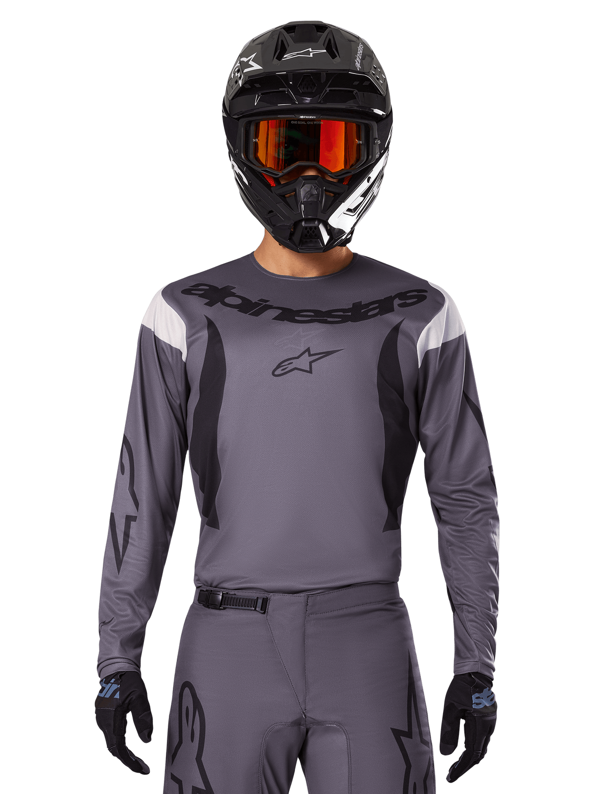 Pilote de motocross portant le maillot et l'ensemble d'équipement Fluid Haul 2025, gris avec des accents noirs et blancs, avec des manches longues et des logos imposants, casque noir avec lunettes orange et gants noirs, tenue coordonnée pour la course tout-terrain