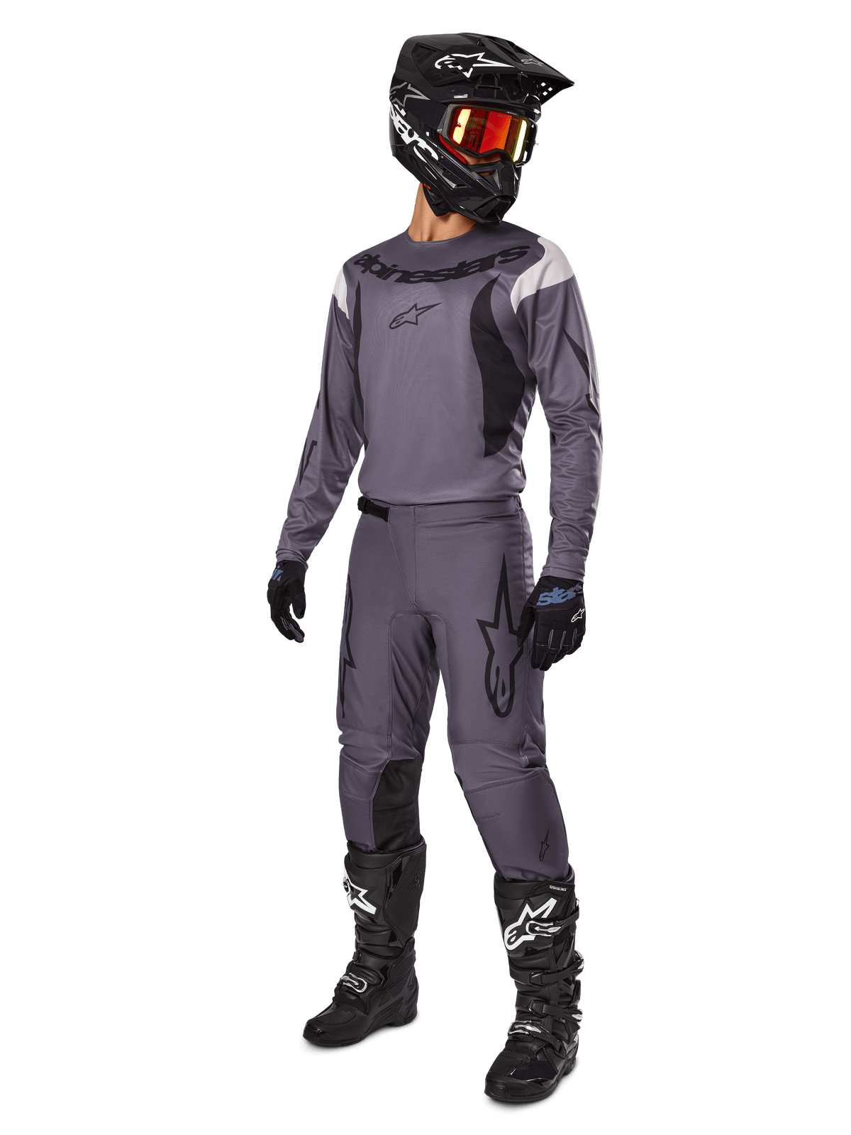 Pilote de motocross portant l'ensemble d'équipement Alpinestars Fluid Haul 2025 en gris, comprenant un maillot et un pantalon gris avec des accents noirs, un casque noir avec des lunettes rougeâtres, des gants noirs et des bottes noires avec des logos blancs, tenue de course tout-terrain complète