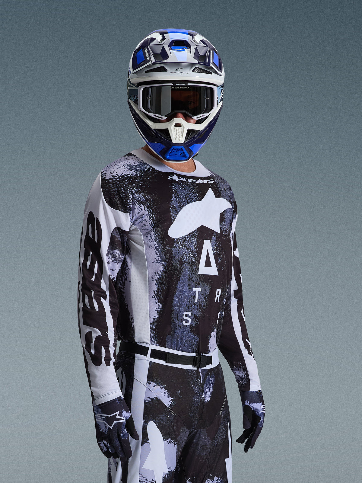 Pilote de motocross portant le maillot Alpinestars Racer Lahnd 2026 en Iron Camo, arborant un motif camouflage noir et gris avec un grand logo Alpinestars blanc sur la poitrine, assorti d'un casque et de gants coordonnés pour la course tout-terrain.