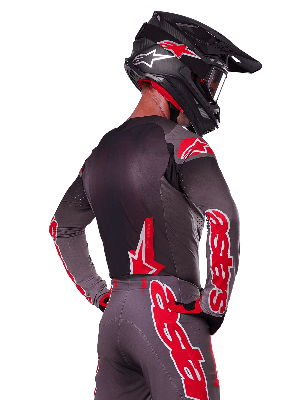 Alpinestars 2025 Supertech Lipan Gear Set, Motocross rider viewed from the back, charcoal grey jersey and pants with vibrant red 'astars' branding on the sleeves and back, paired with a black helmet
