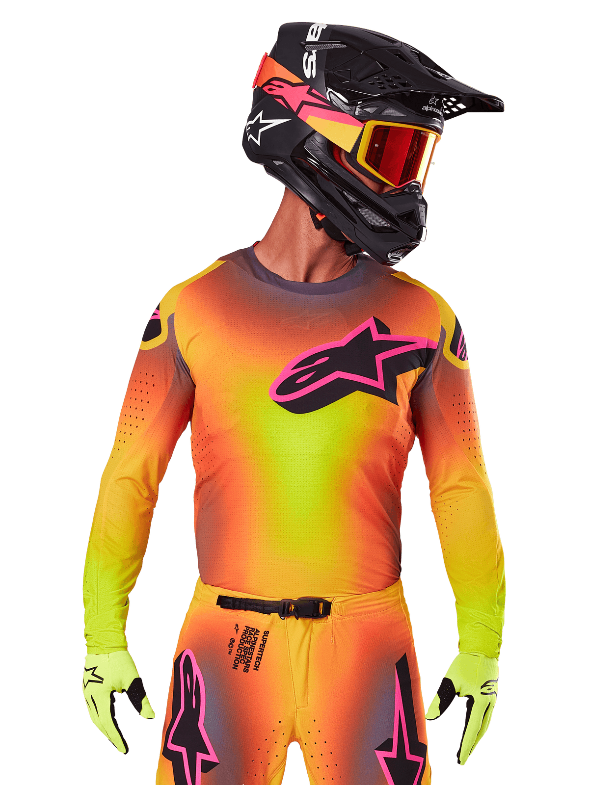 Pilote de motocross portant le maillot Supertech Lipan 2025, dégradé éclatant de jaune, orange et rose, grand logo étoile Alpinestars noir avec contour rose sur la poitrine, perforations découpées au laser pour la ventilation, coupe de course athlétique, avec un pantalon assorti, des gants jaunes et un casque noir avec des lunettes.