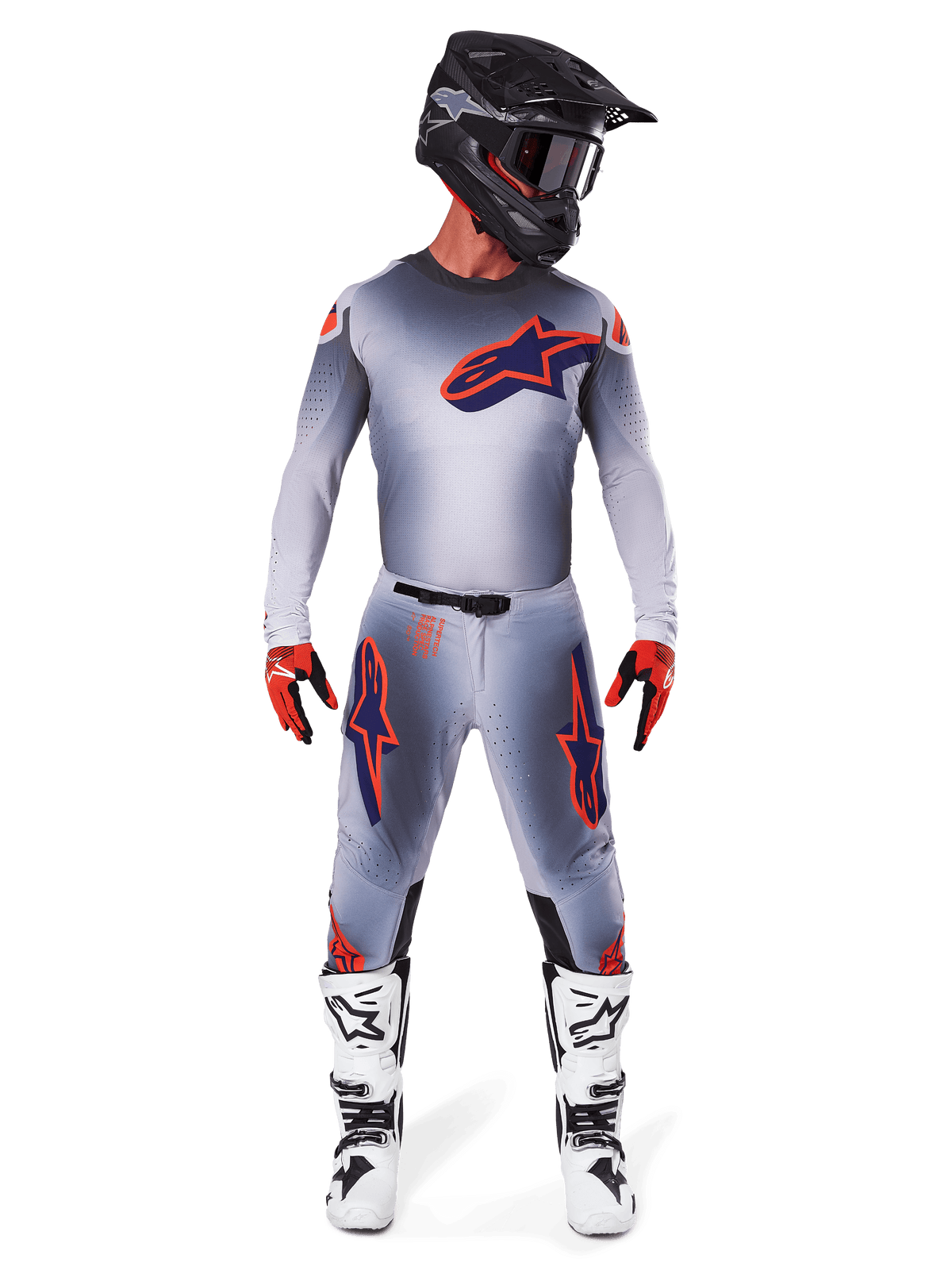 Motocross rider wearing the 2025 Supertech Lipan Gear Set in Gray Orange Fluo, featuring a gray jersey with orange accents and a navy Alpinestars logo, matching gray pants with large thigh logos, a matte black helmet, white and black boots, and red and black gloves, complete pro-level racing outfit.