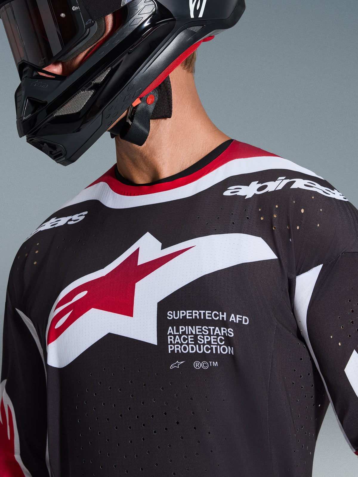 Maillot Alpinestars Supertech AFD Vista 2026, noir, rouge et blanc, gros plan sur le buste montrant le logo étoile Alpinestars et l'inscription « Supertech AFD », doté de perforations de ventilation découpées au laser, porté avec un casque de motocross noir.