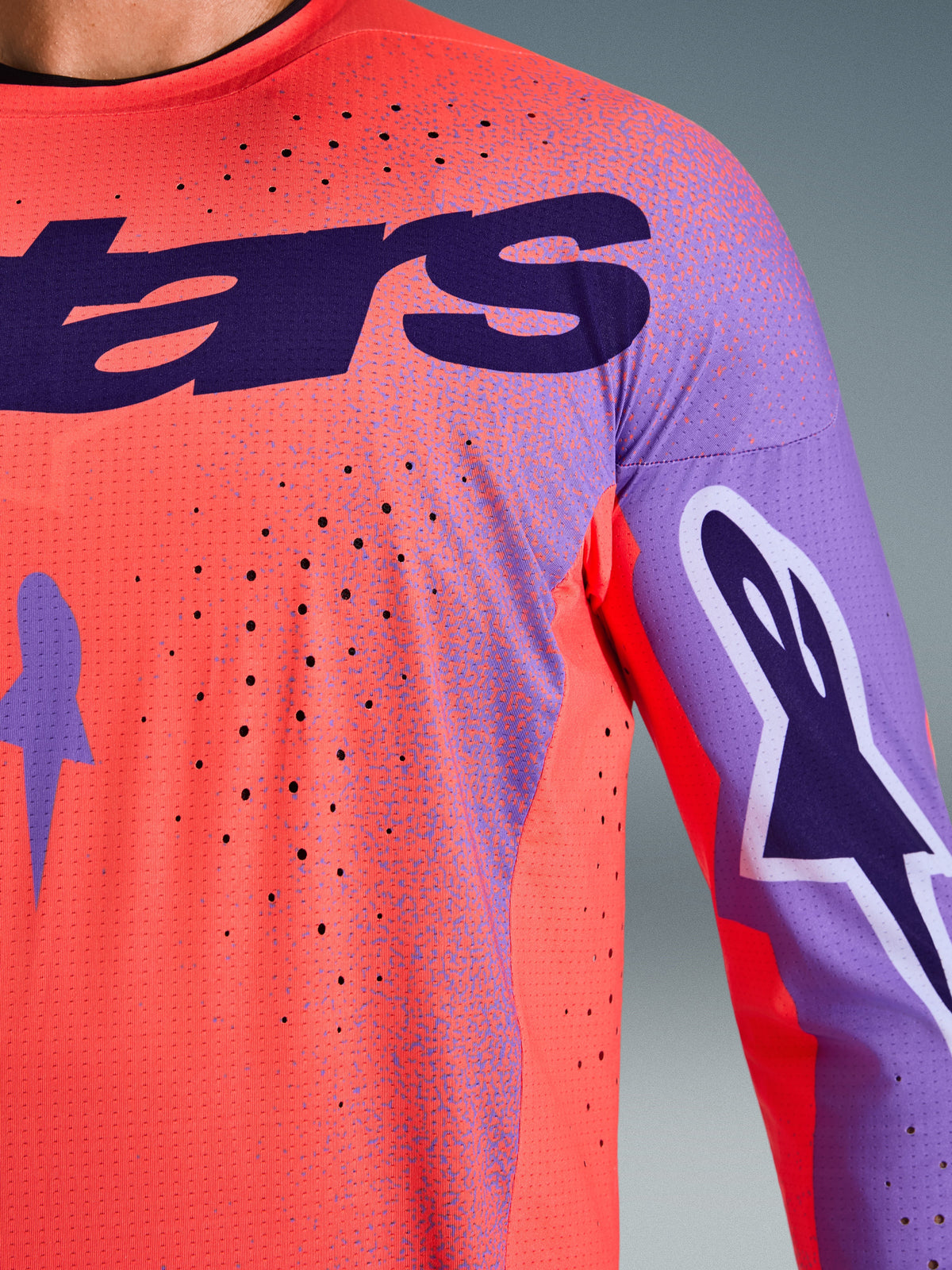 Maillot Alpinestars Supertech Scenz 2026, maillot de motocross, corail vif et violet, vue rapprochée montrant la texture en maille respirante et les perforations découpées au laser, avec un grand logo violet sur la poitrine et des graphismes sur les manches pour la compétition tout-terrain professionnelle.