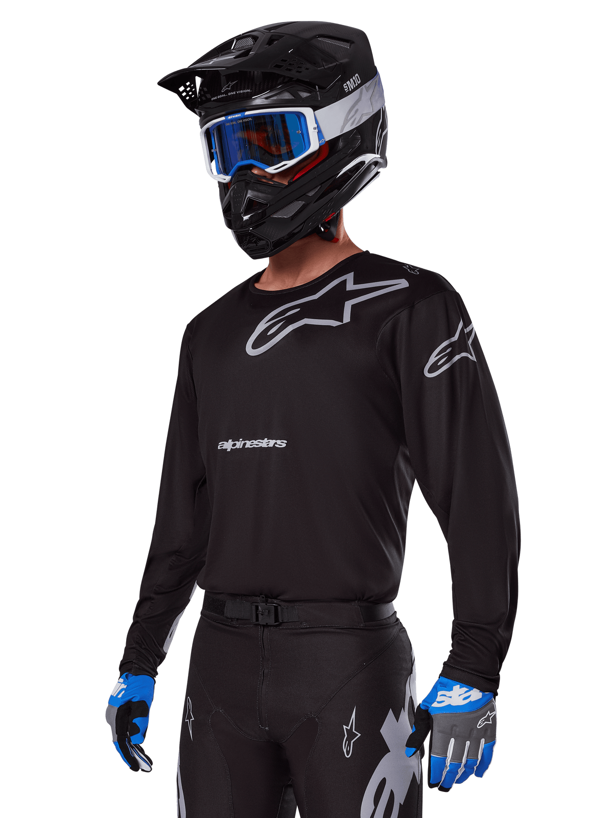 Pilote de motocross portant l'ensemble d'équipement Alpinestars Racer Graphite 2025, maillot noir avec logos Alpinestars gris, pantalon noir assorti avec accents gris, casque noir avec lunettes bleues et blanches, gants bleus et gris, tenue technique épurée pour la course tout-terrain