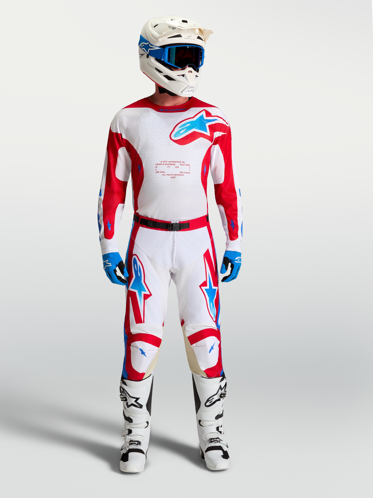 Maillot Alpinestars Racer Hunt, maillot de motocross pour homme blanc et rouge avec accents bleus, porté avec pantalon et bottes de moto assortis, équipement tout-terrain de performance.