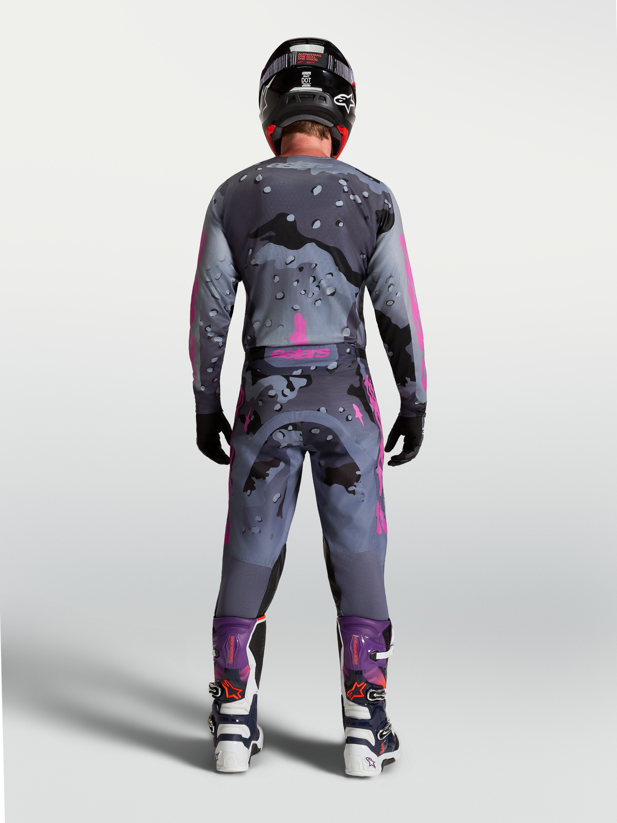 Alpinestars Racer Lone Gear Set, tenue de motocross pour homme grise et violette, motif camouflage, pilote vu de dos.