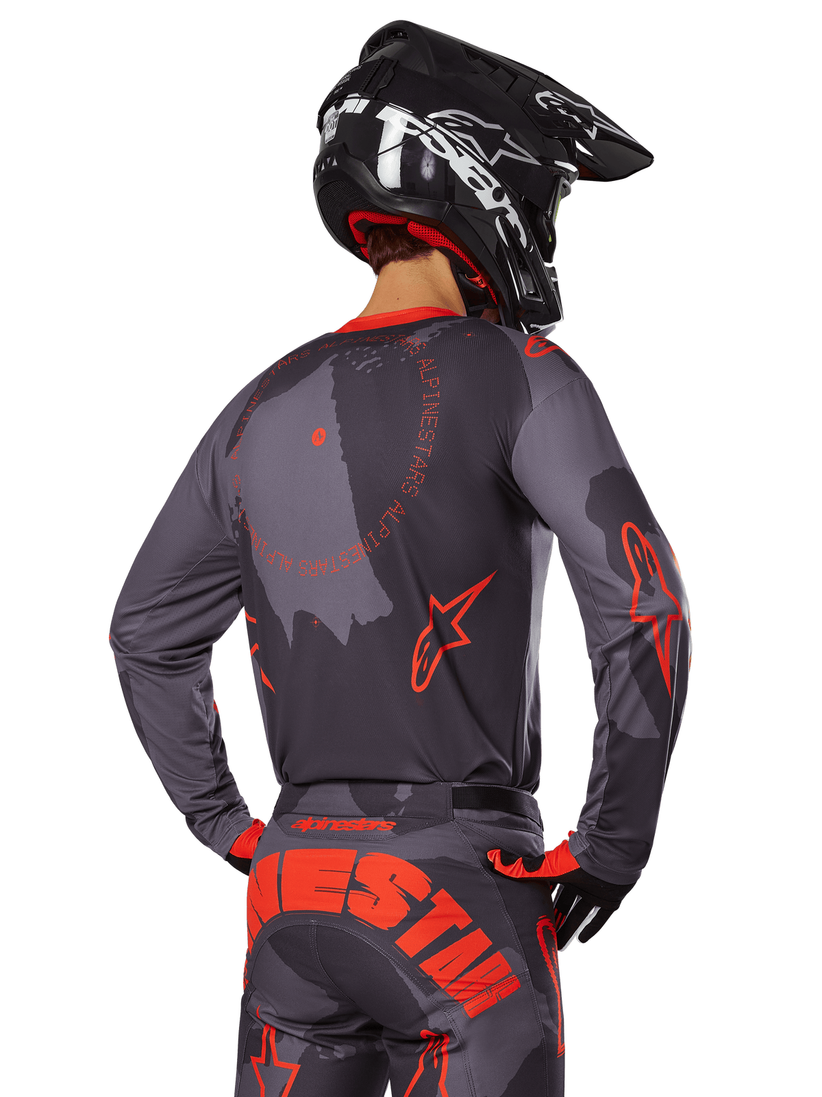 Alpinestars 2025 Racer Hollow Jersey, back view of a motocross rider in Gray Camo and Orange Fluo gear, featuring matching camo pants with large orange Alpinestars lettering and a black helmet, professional off-road apparel design