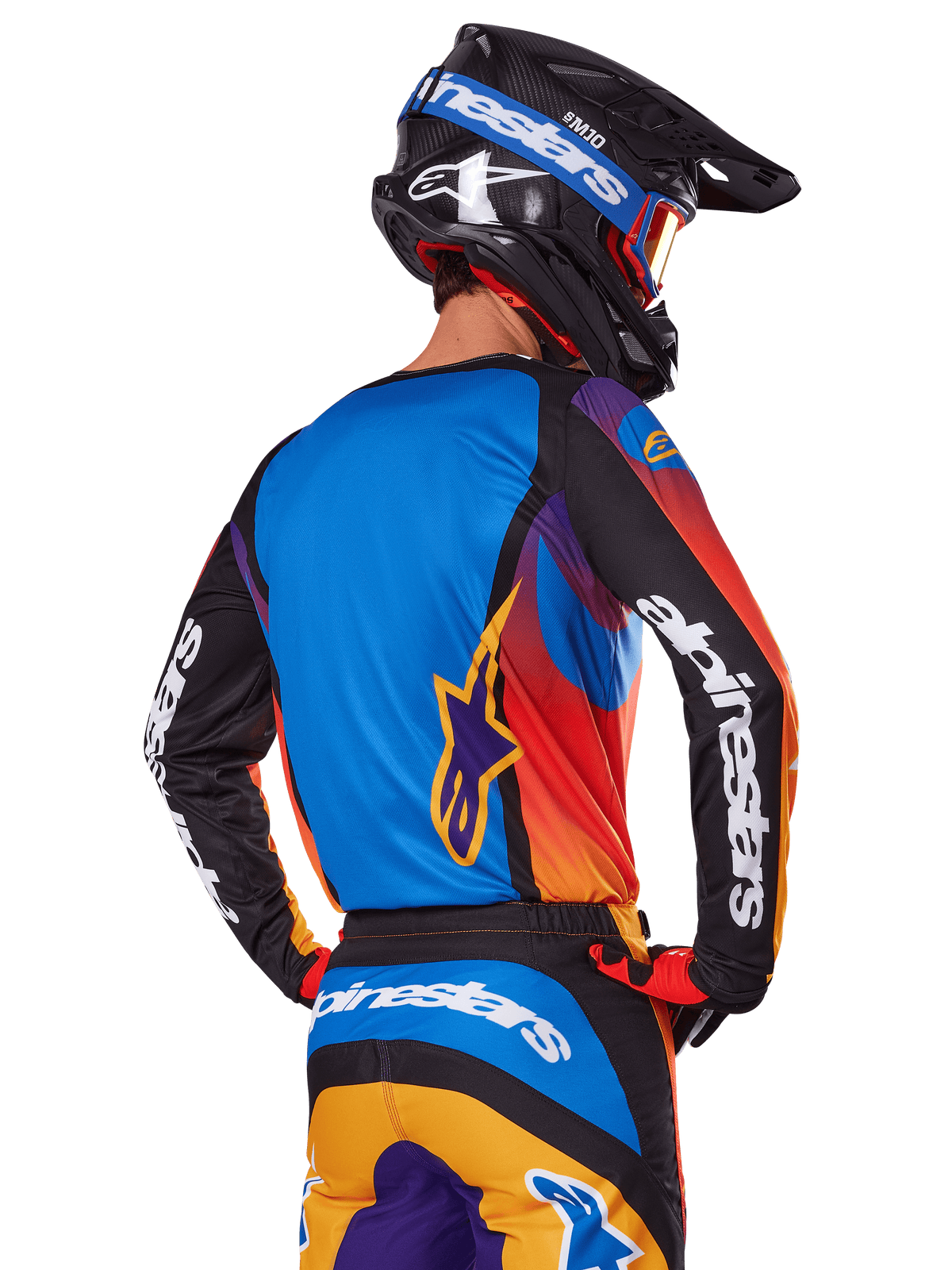 Motocross rider viewed from the back wearing the Alpinestars 2025 Fluid Wurx Gear Set, multicolor jersey with blue back and black sleeves featuring white logos, matching orange and blue pants, black and blue helmet with orange goggles, coordinated off-road racing outfit.