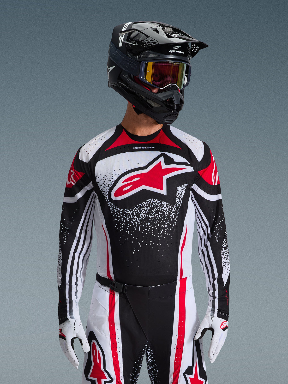 Ensemble d'équipement Alpinestars Techstar Nomur 2026, maillot et pantalon de motocross, noir, blanc et rouge, avec un grand logo rouge sur la poitrine et un motif graphique moucheté, porté avec un casque noir, des lunettes rouges et des gants blancs, coupe athlétique de course professionnelle pour le tout-terrain.