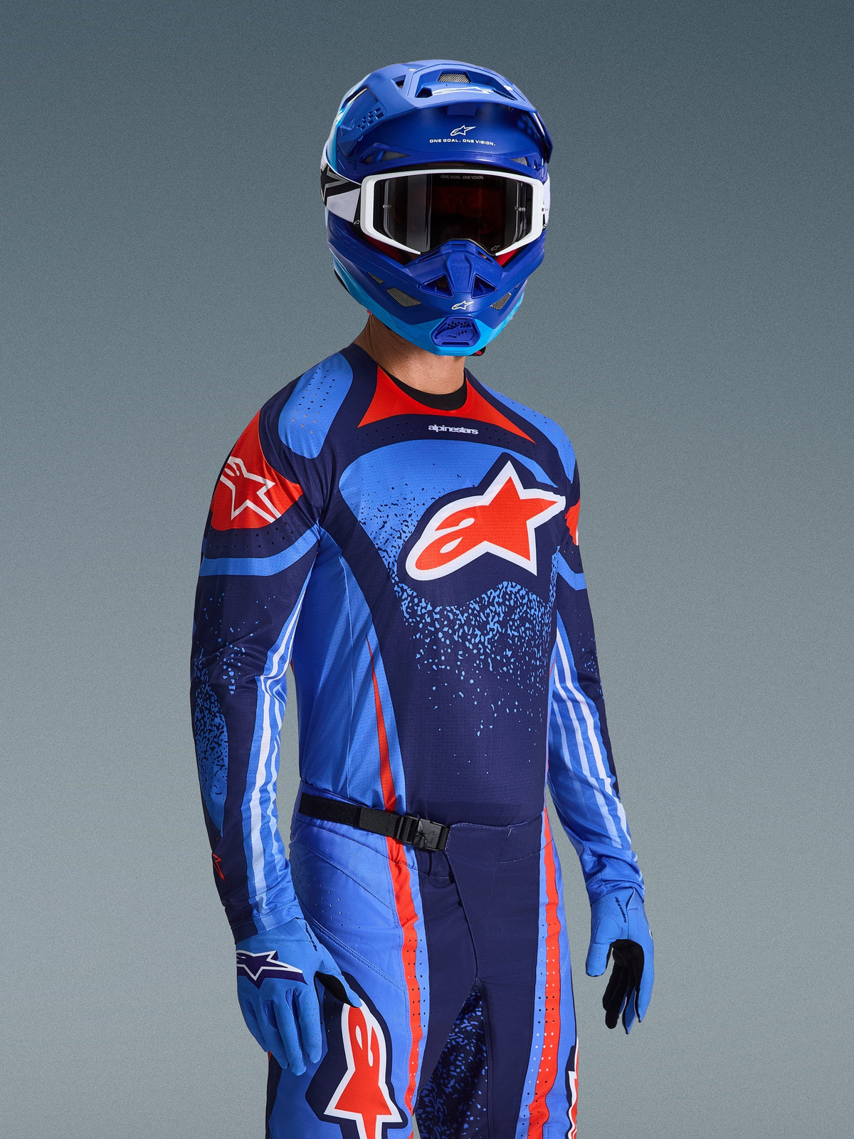 Ensemble d'équipement Alpinestars Techstar Nomur 2026, maillot et pantalon de motocross bleu marine foncé, orange et bleu UCLA, porté par un pilote avec casque et gants bleus assortis, présentant des graphismes de logo audacieux et une coupe athlétique de course.