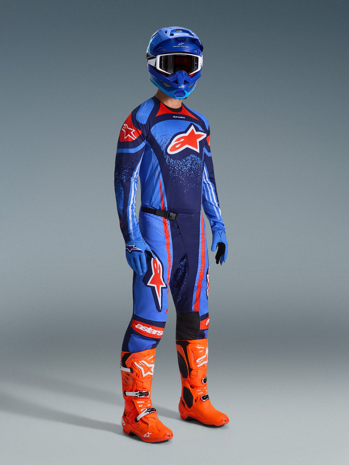 Pilote de motocross portant l'ensemble d'équipement Techstar Nomur 2026, maillot bleu marine avec des accents bleu clair et orange, pantalon assorti à rayures orange, casque de course bleu, bottes orange vif et gants bleus, tenue de motocross coordonnée pour la performance tout-terrain