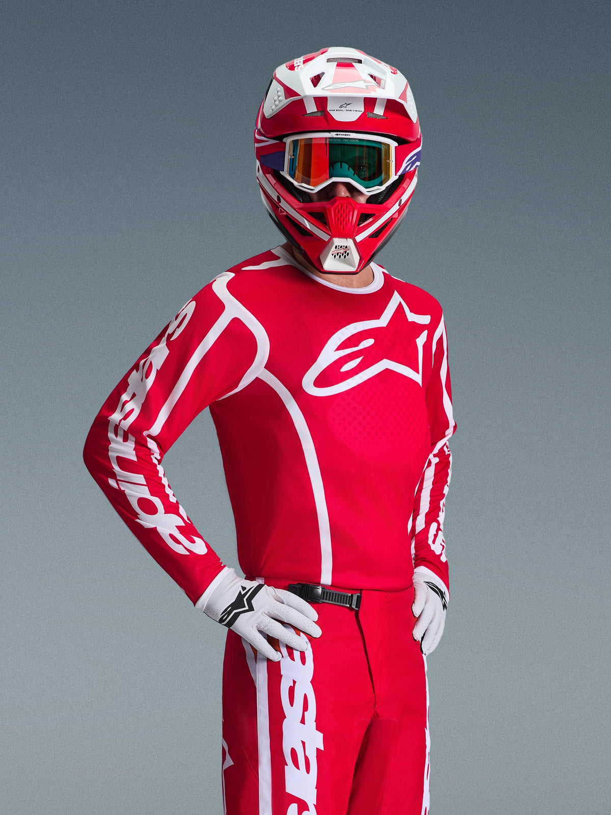 Pilote de motocross portant l'ensemble d'équipement Alpinestars 2026 Fluid Apex rouge et blanc, comprenant un maillot rouge avec logos blancs, un pantalon assorti, des gants blancs et un casque rouge et blanc avec lunettes irisées, tenue de course tout-terrain coordonnée