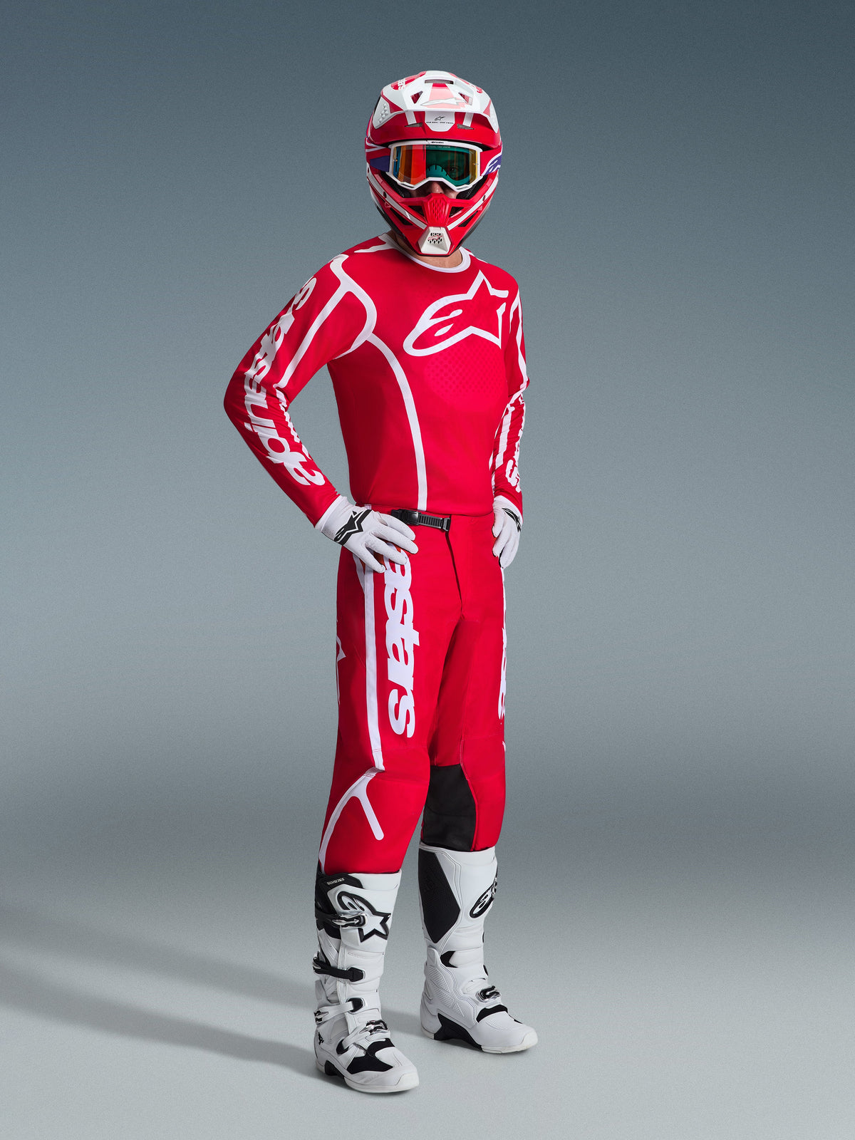 Pilote de motocross portant la tenue Alpinestars 2026 Fluid Apex, maillot rouge avec grands logos blancs, pantalon rouge assorti avec marquage blanc, casque blanc et rouge, bottes et gants de motocross blancs, tenue coordonnée pour la course tout-terrain
