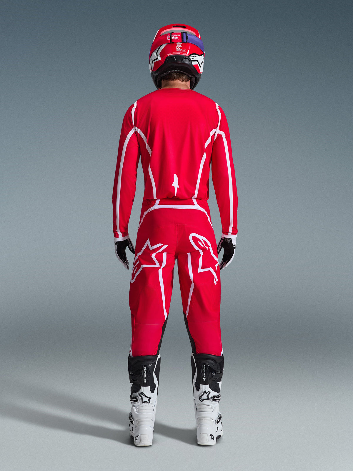 Vue arrière d'un pilote de motocross portant l'ensemble Alpinestars 2026 Fluid Apex, maillot et pantalon rouge vif avec bandes et logos blancs, bottes blanches et noires et casque rouge, tenue de course tout-terrain professionnelle