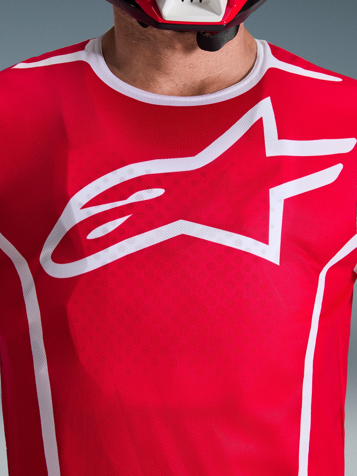 Gros plan du maillot Alpinestars 2026 Fluid Apex en rouge et blanc, présentant un grand logo Astars blanc sur la poitrine, une construction en maille de poly-tissu respirant et une bordure de col blanche, vêtement de course de motocross.