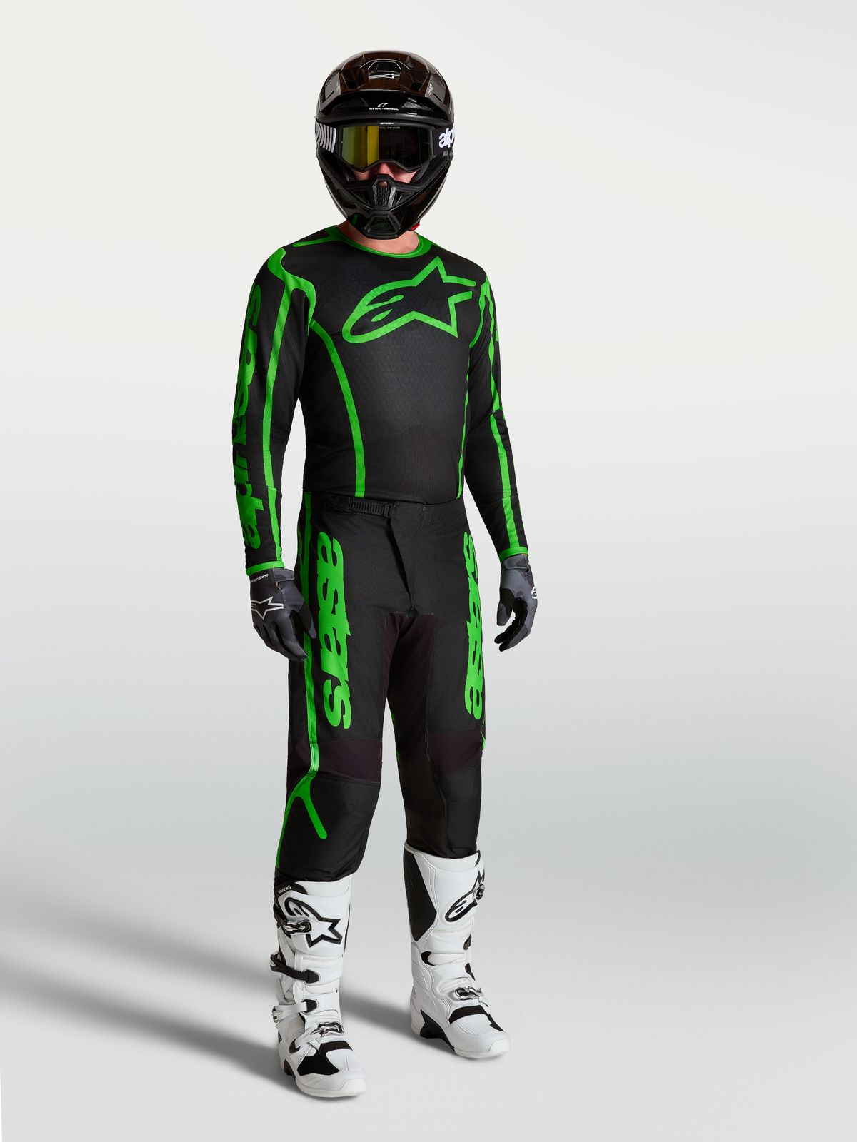 Maillot Fluid Apex V2 Alpinestars, maillot de motocross pour homme, noir et vert fluo, porté avec pantalon et bottes assortis.