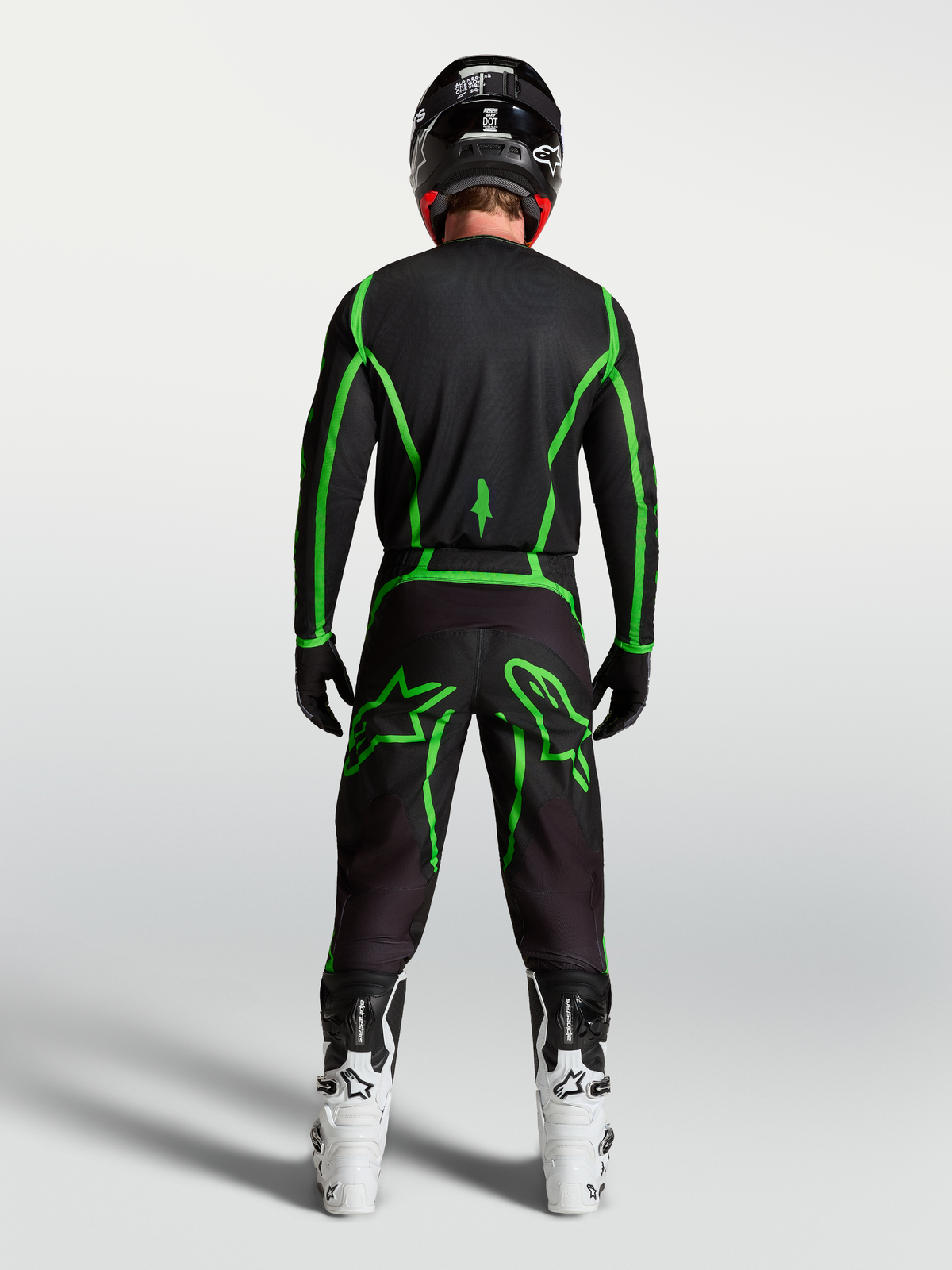 Maillot Alpinestars Fluid Apex V2 de motocross, noir et vert fluo, vue de dos sur un pilote avec des bottes blanches.