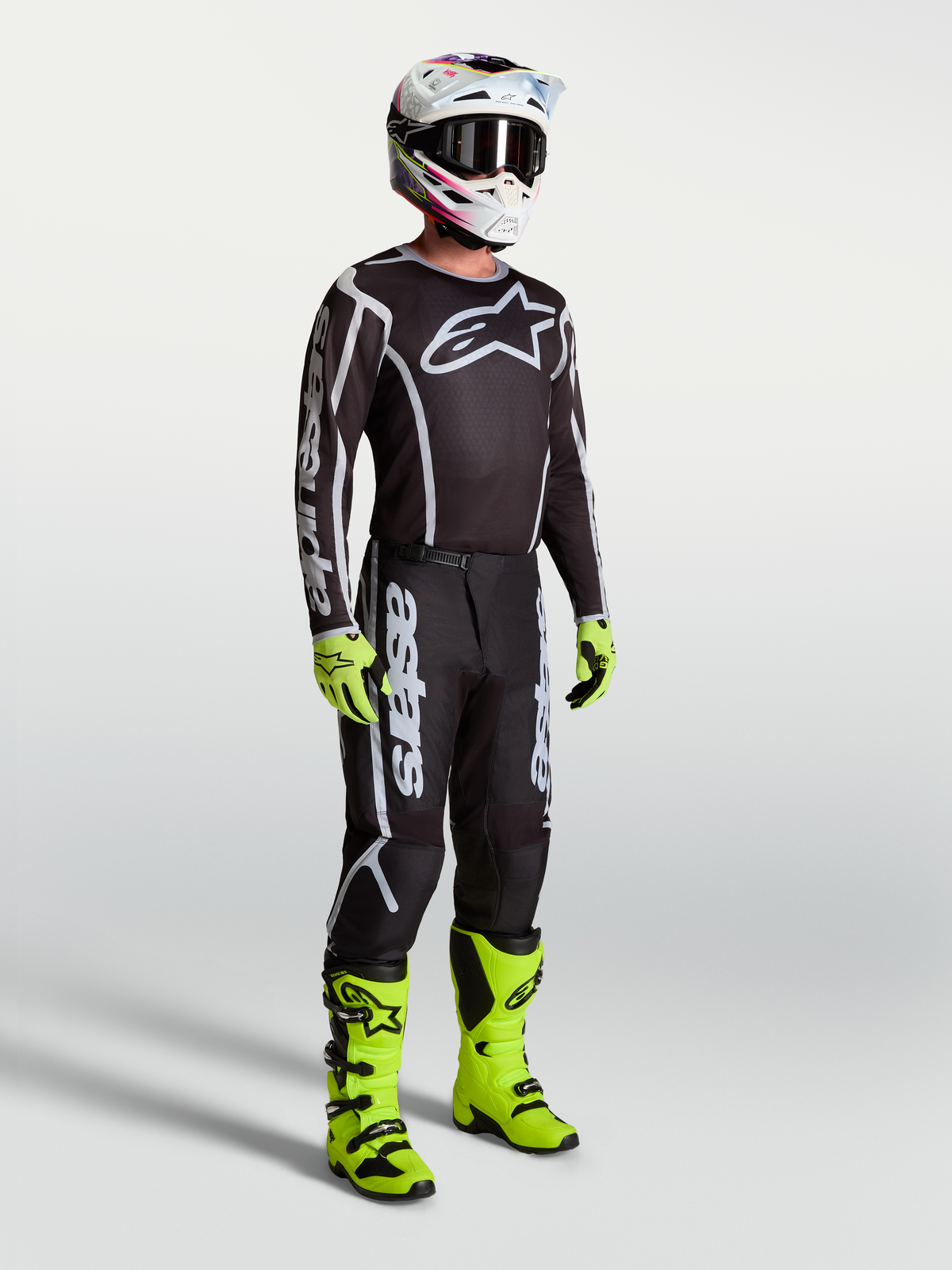 Maillot Alpinestars Fluid Apex V2, maillot de motocross pour homme, noir et argenté, porté avec des bottes et gants vert fluo.