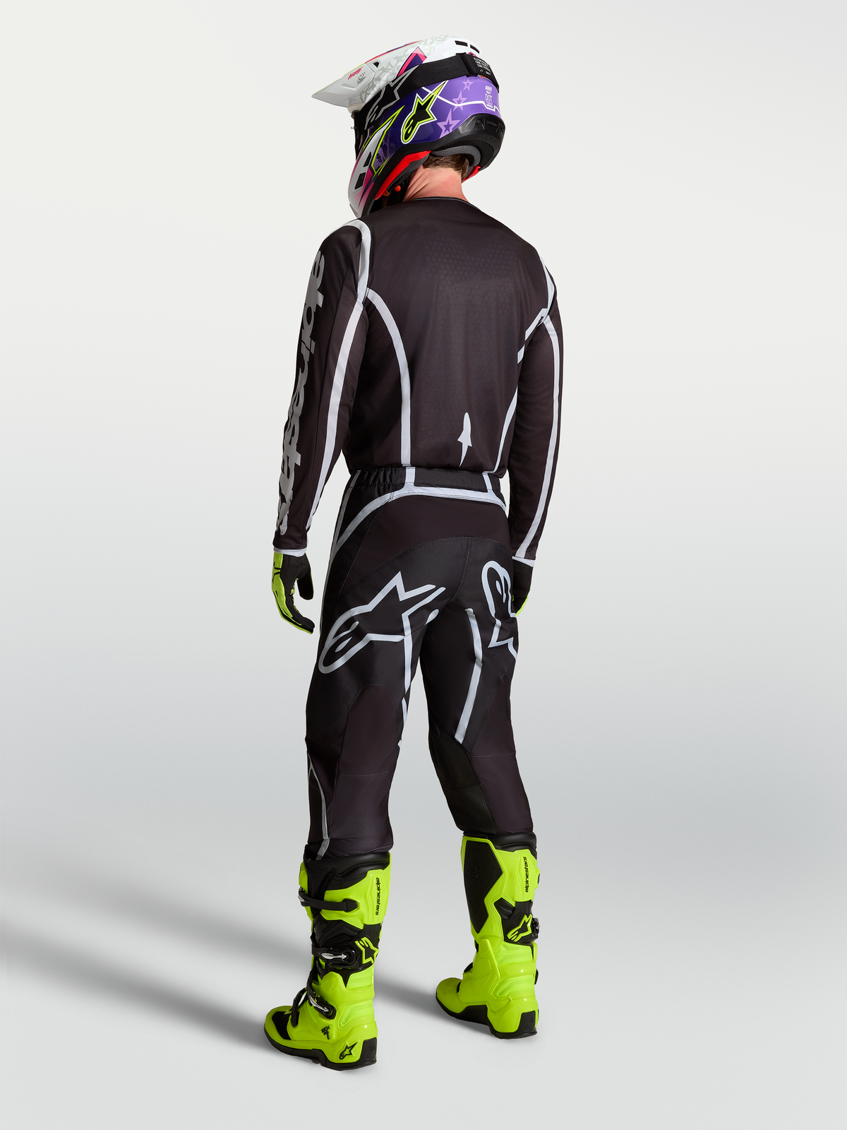 Maillot Fluid Apex V2 d'Alpinestars, maillot de motocross pour homme, noir et argenté, coupe performance vue de dos sur un pilote en tenue complète, conçu pour la conduite tout-terrain.