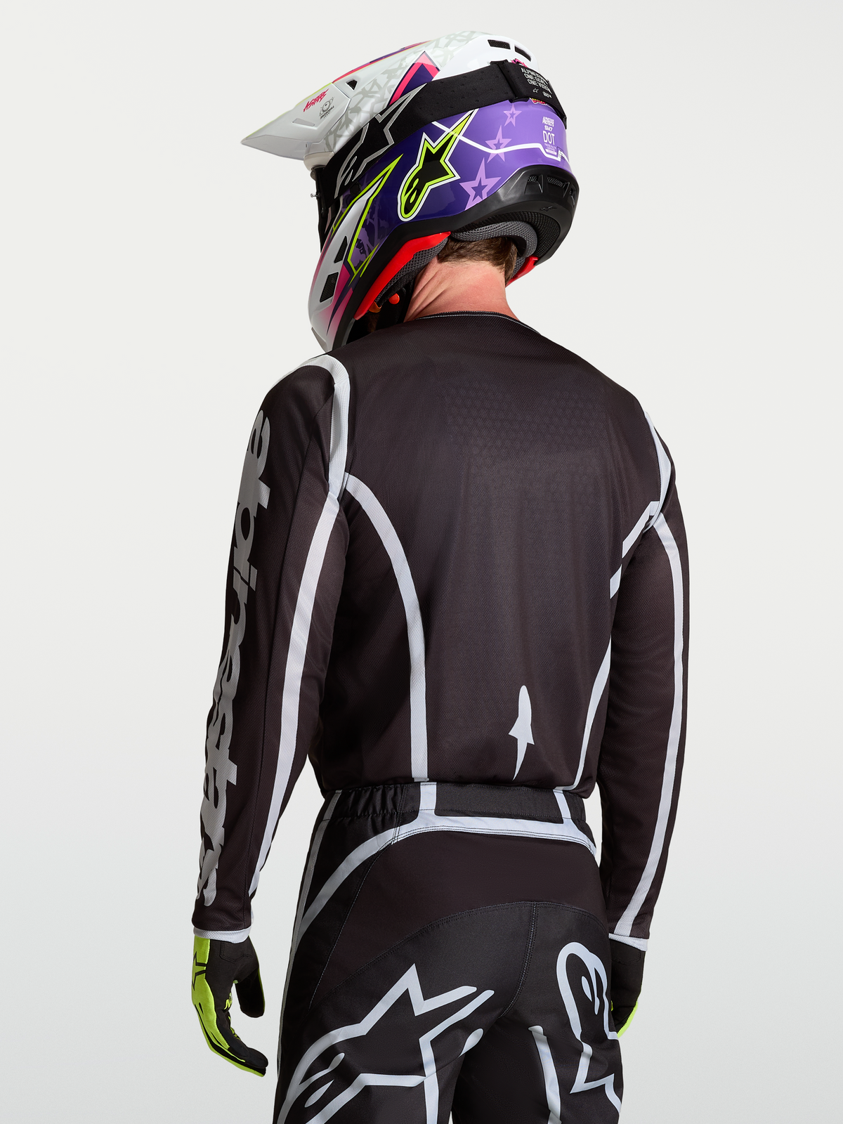 Maillot Fluid Apex V2 d'Alpinestars, haut de motocross pour homme, noir et argenté, vu de dos sur un mannequin avec casque, en poly-tissu évacuant l'humidité
