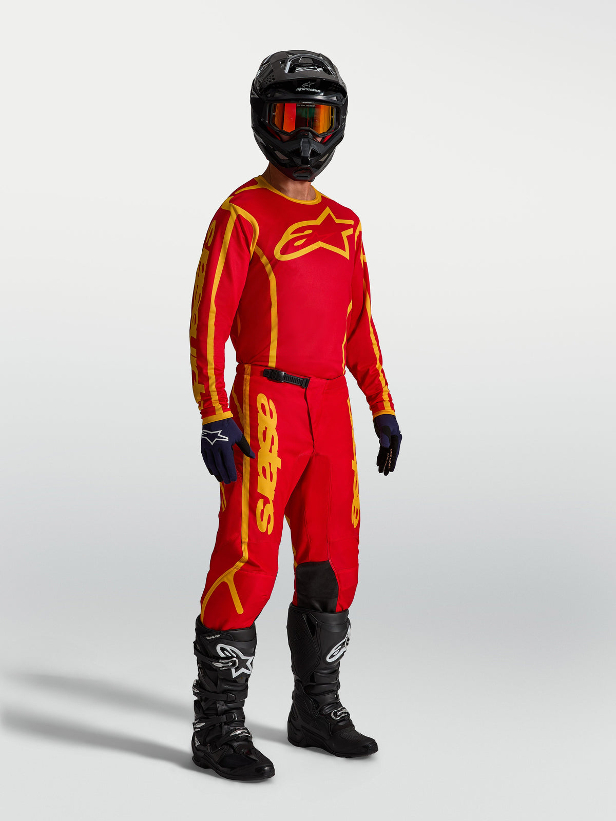Maillot Alpinestars Fluid Apex V2, maillot de motocross rouge et doré pour homme, respirant, porté avec tenue complète.