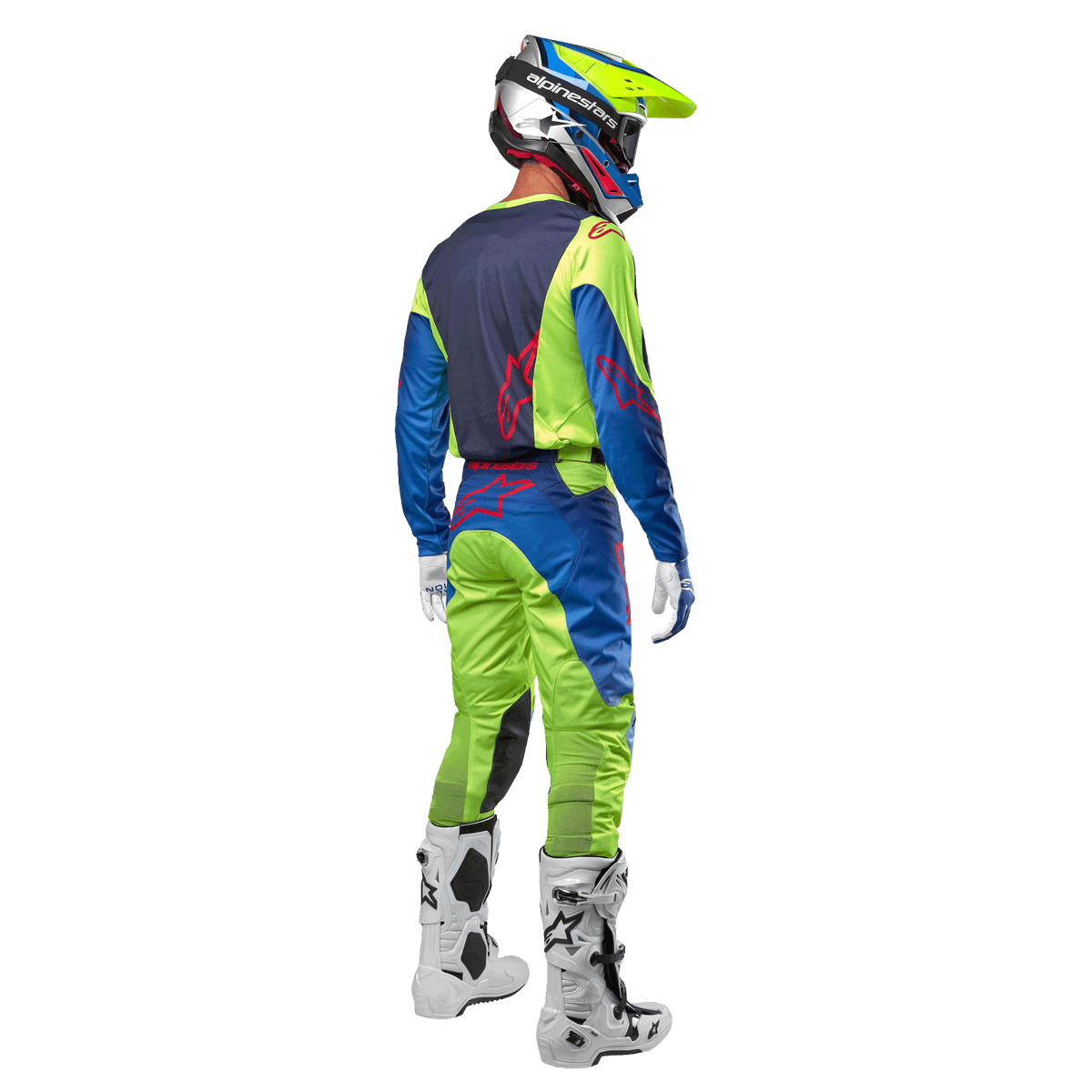 Pilote de motocross de dos portant le maillot Alpinestars Racer Hoen 2024 en jaune fluo et bleu marine, avec pantalon de motocross assorti et bottes blanches, montrant le design arrière avec logos rouges, tenue coordonnée pour la course tout-terrain professionnelle
