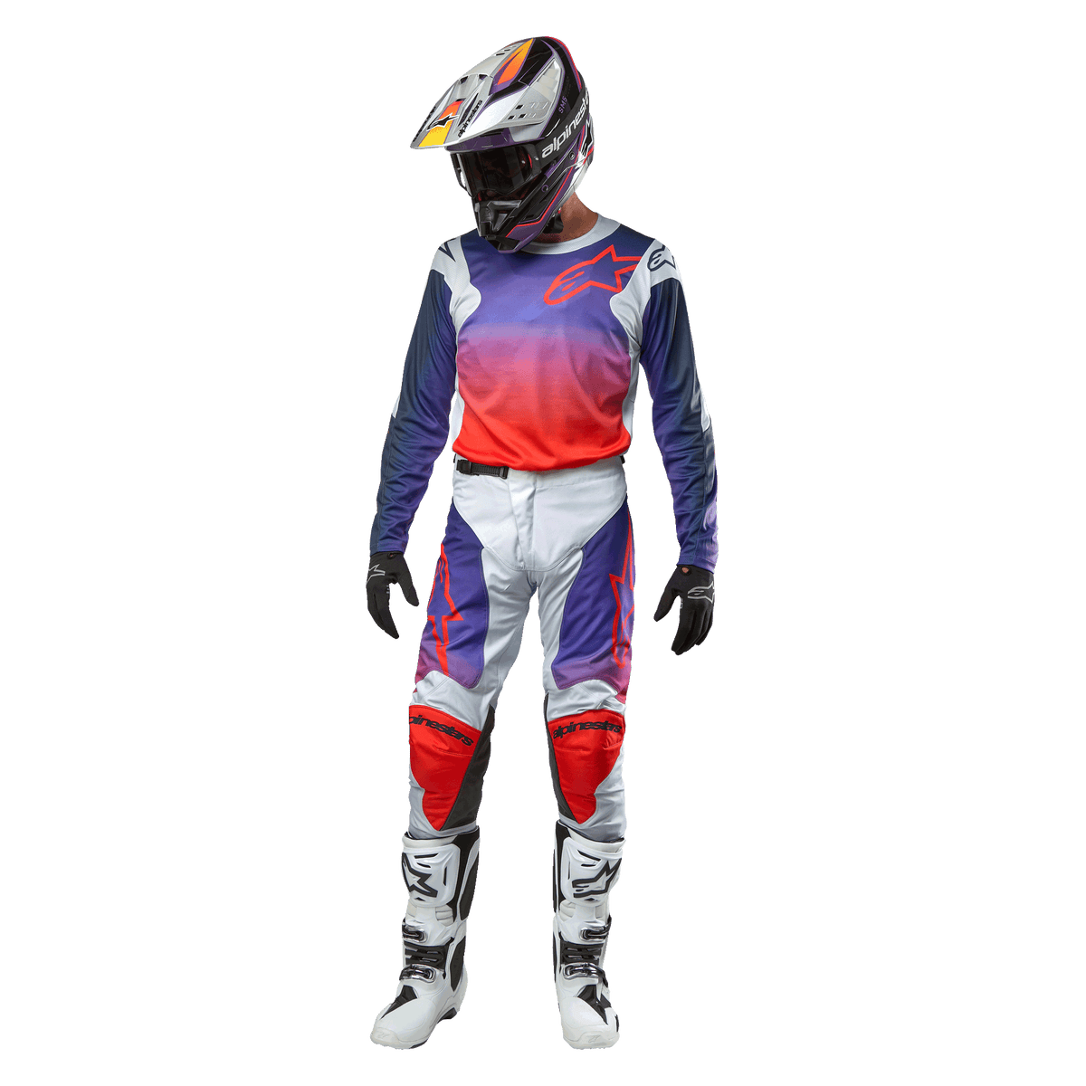 Pilote de motocross portant une tenue de course complète, maillot Alpinestars Racer Hoen 2024 avec dégradé du violet à l'orange vif et épaules gris clair, pantalon gris clair assorti avec accents rouges et violets, casque coordonné et bottes blanches, tenue de course tout-terrain complète