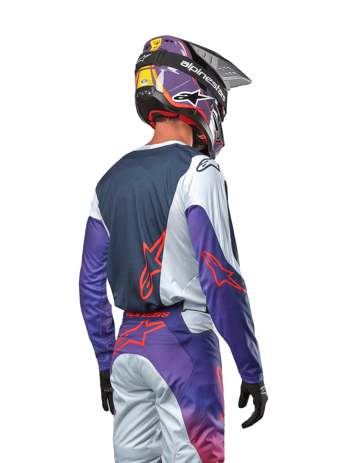 Pilote de motocross vu de dos portant le Maillot Racer Hoen 2024, panneau arrière bleu marine avec épaules gris clair et manches violettes, logos Alpinestars orange vif, pantalon assorti violet et gris avec un casque de motocross violet, tenue de course tout-terrain complète