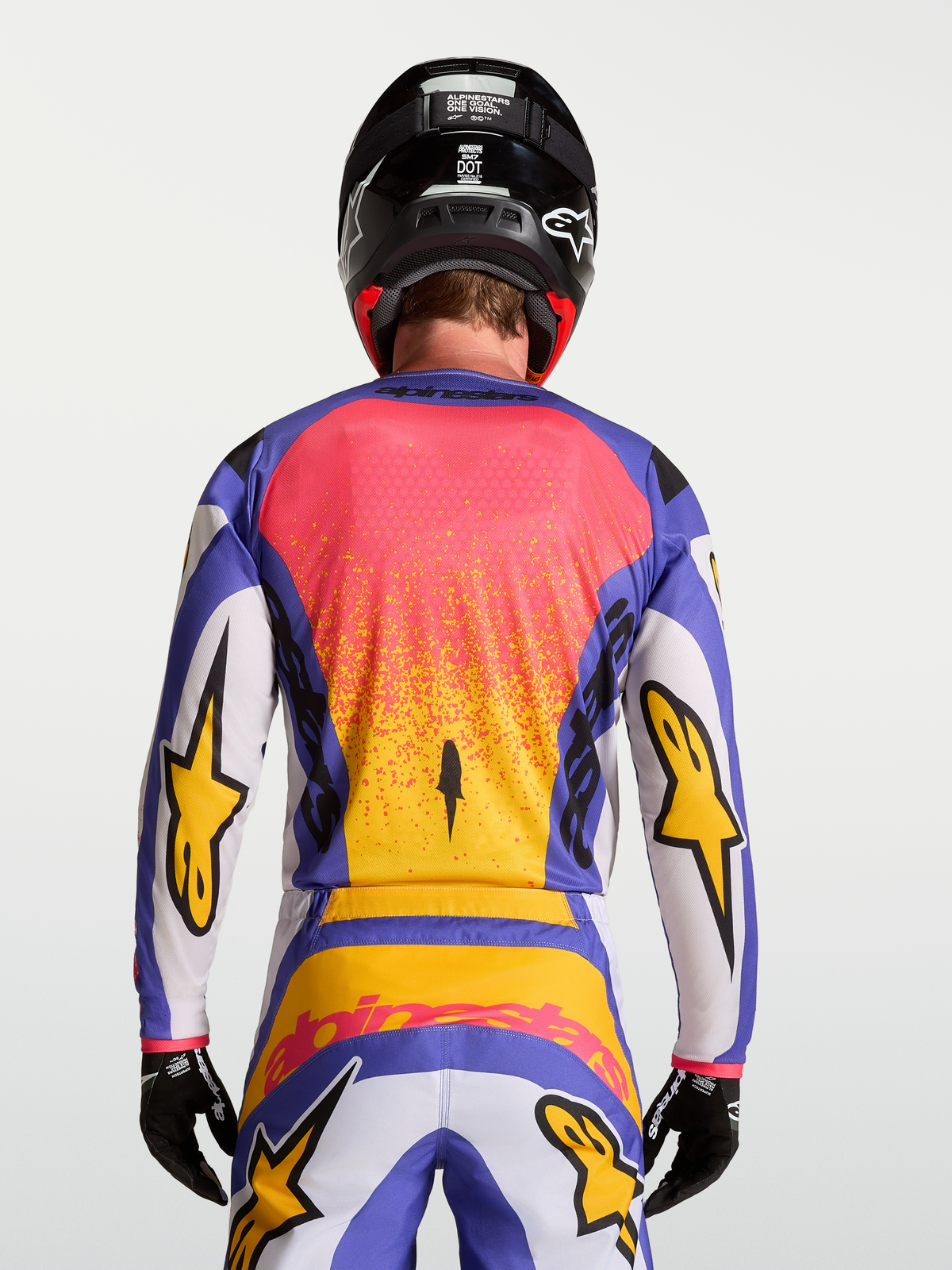 Maillot Fluid Drag Alpinestars, haut de motocross tout-terrain pour homme, lilas clair et bleu avec accents dorés, vue de dos portée par un mannequin avec casque et gants assortis