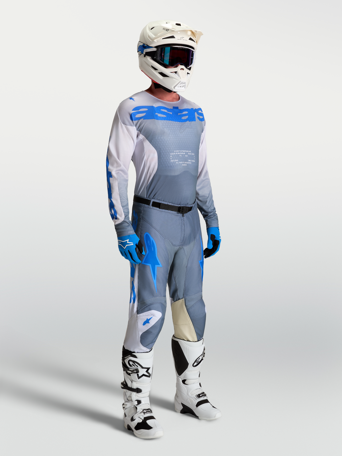 Maillot Racer Amber Alpinestars, tenue de motocross pour homme, gris cendré et bleu, porté par un mannequin avec casque et bottes de performance.