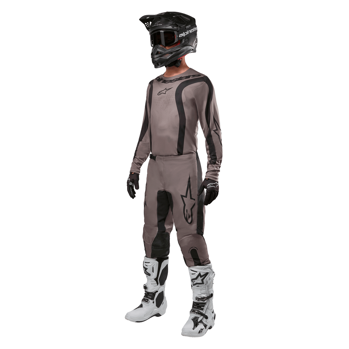 Pilote de motocross portant un équipement de course complet comprenant le maillot Alpinestars 2024 Fluid Lurv en Mud Black, associé à un pantalon assorti, un casque noir avec lunettes, des bottes blanches et noires et des gants noirs, tenue coordonnée pour la course tout-terrain