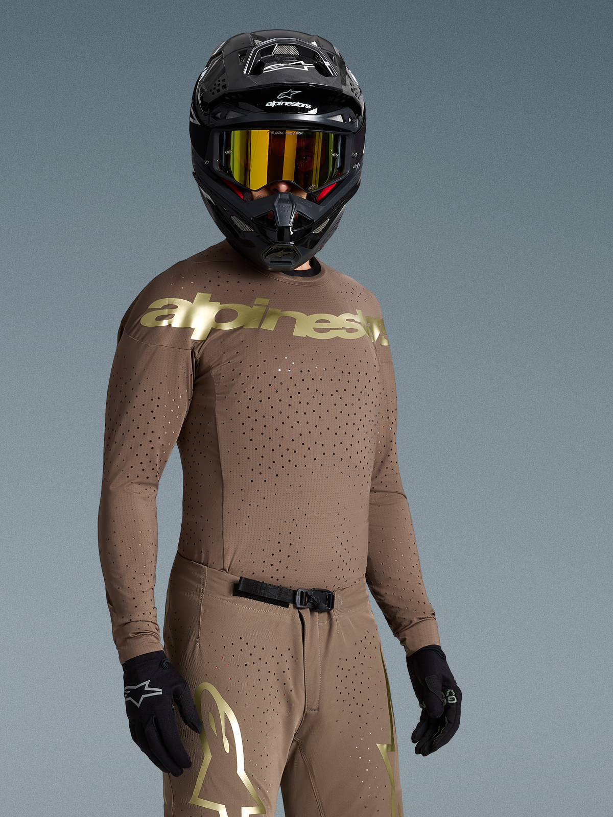 Tenue complète Alpinestars Supertech Air Gold Édition Limitée, ensemble de motocross marron et doré avec ventilations laser, porté par un pilote.