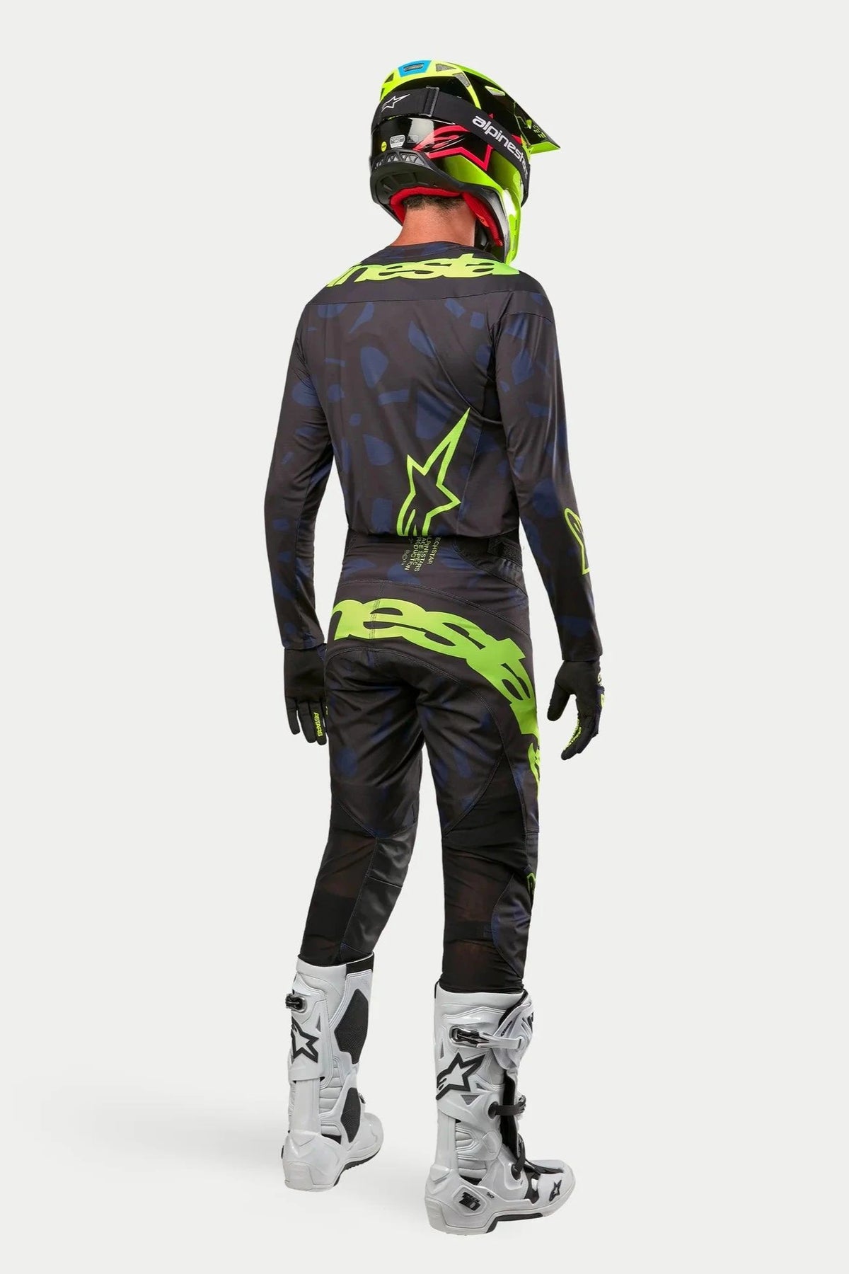 Ensemble maillot et pantalon Alpinestars Techstar Rantera 2024, pilote de motocross en tenue complète vu de dos, noir, bleu marine et jaune fluo, avec casque jaune fluo assorti et bottes blanches, tenue de course tout-terrain coordonnée