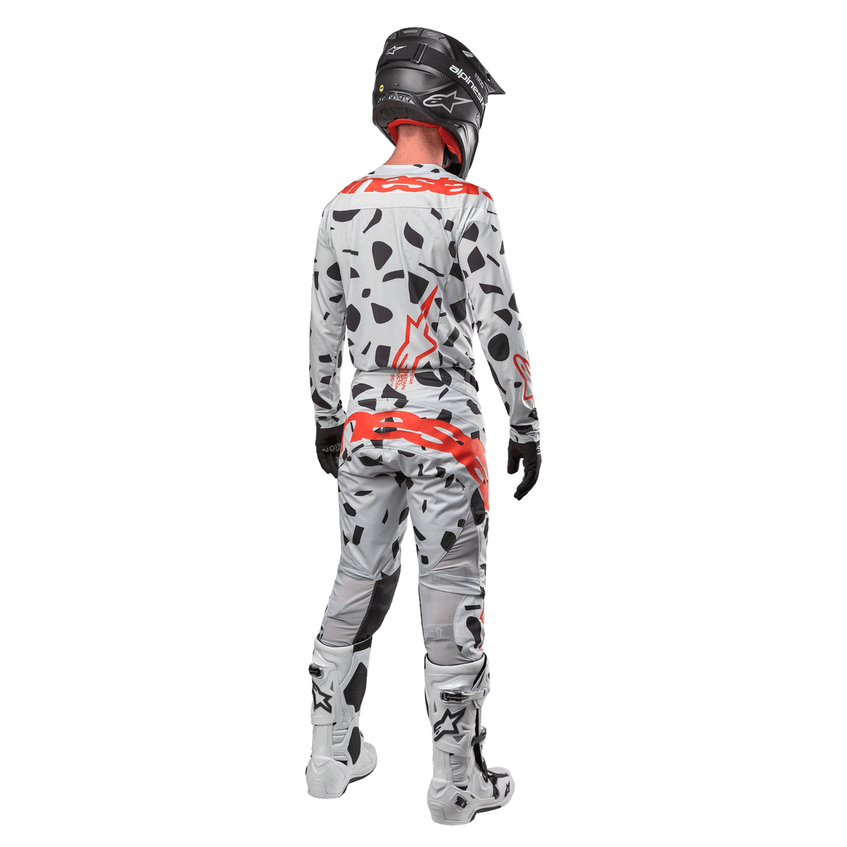 Pilote de motocross vu de dos portant le maillot Alpinestars Techstar Rantera 2024 et le pantalon assorti, motif camouflage Haze Gray avec logos Alpinestars rouges, casque noir, bottes blanches et noires, gants noirs, tenue de motocross coordonnée.