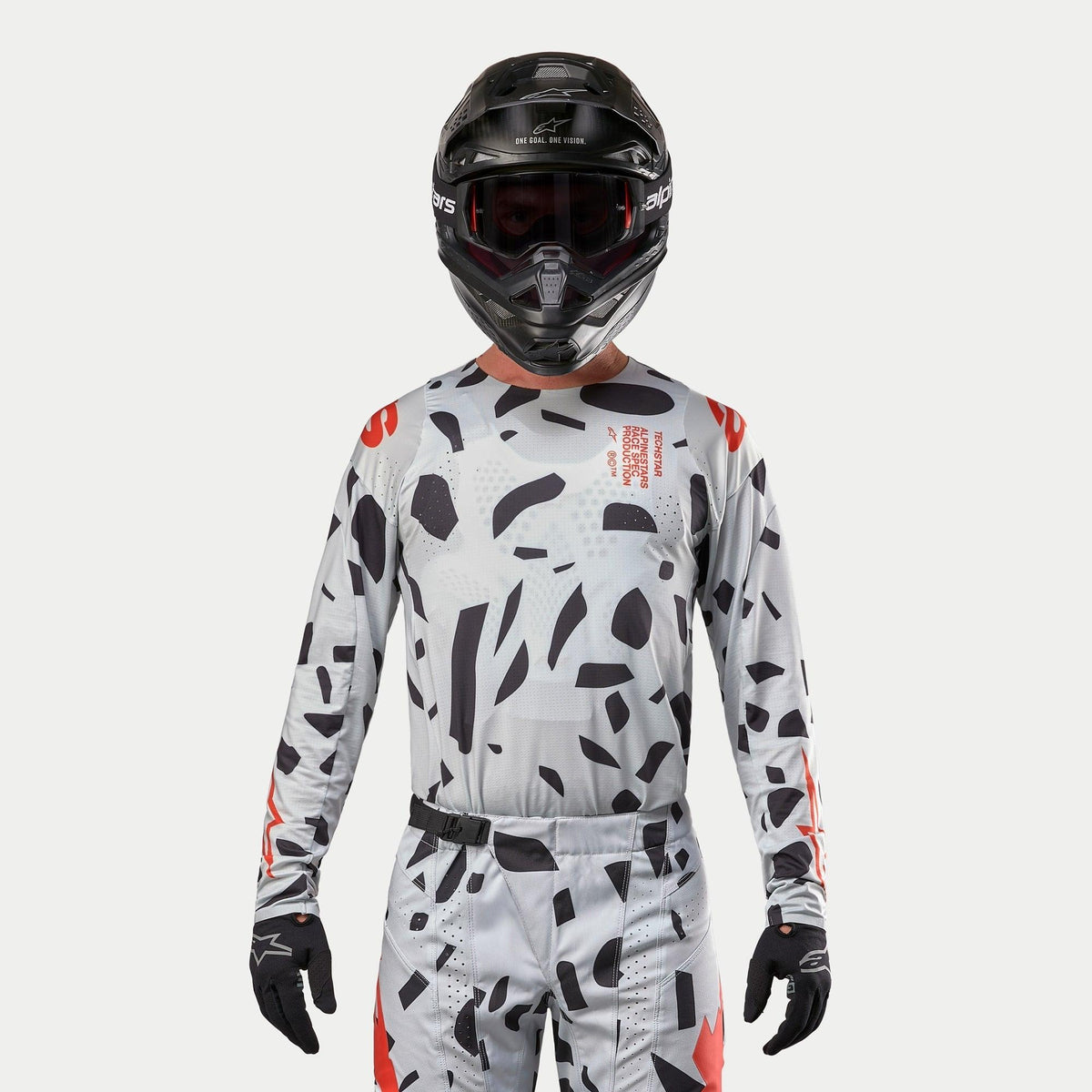 Maillot Alpinestars Techstar Rantera 2024, maillot de motocross, camouflage Haze Gray avec motifs noirs irréguliers et accents rouges, porté par un pilote avec pantalon assorti, casque noir et gants, équipement de course tout-terrain