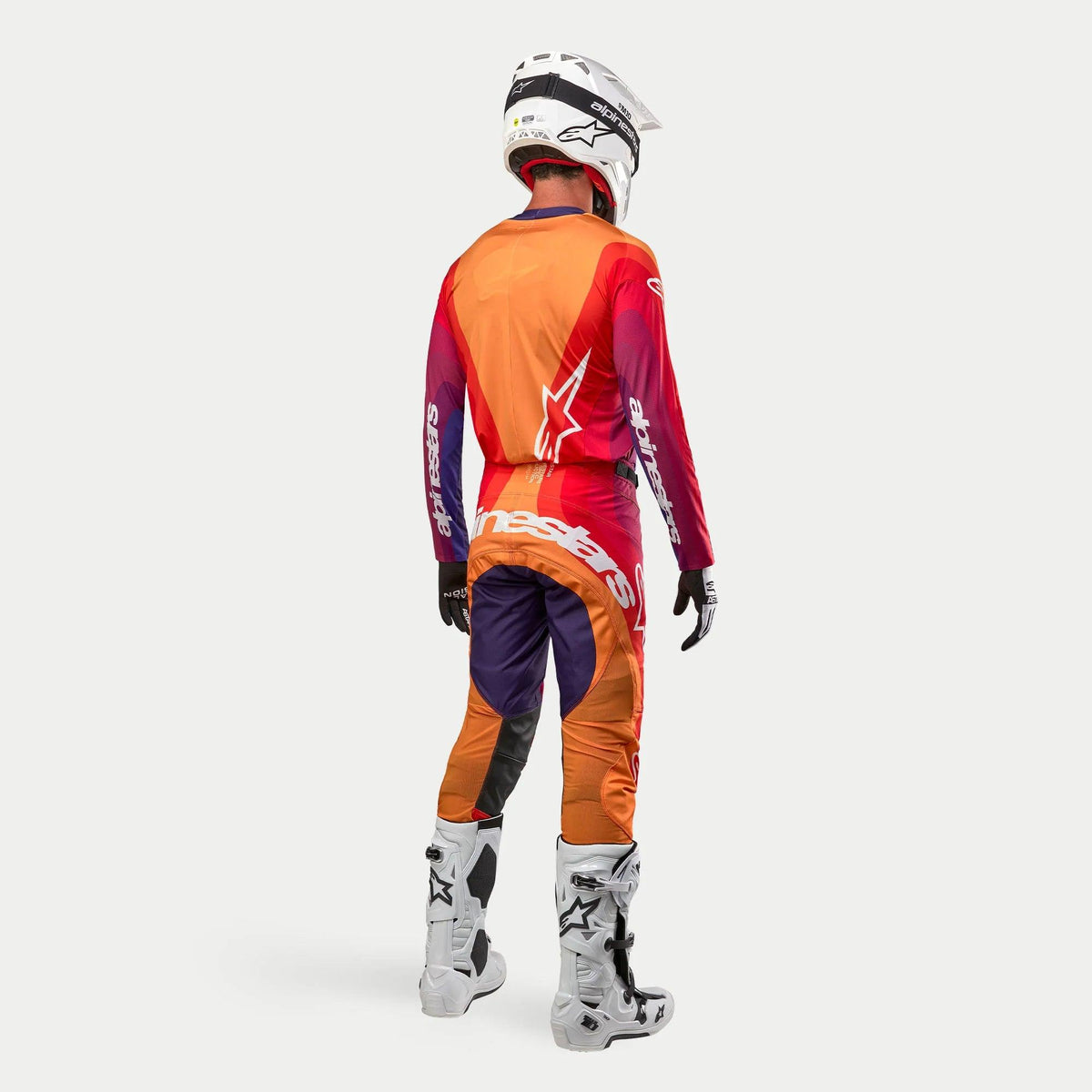Alpinestars 2024 Techstar Pneuma, tenue de motocross complète, vue de dos, maillot et pantalon violet, orange et bleu foncé, casque blanc, bottes blanches, équipement de sport motorisé haute performance
