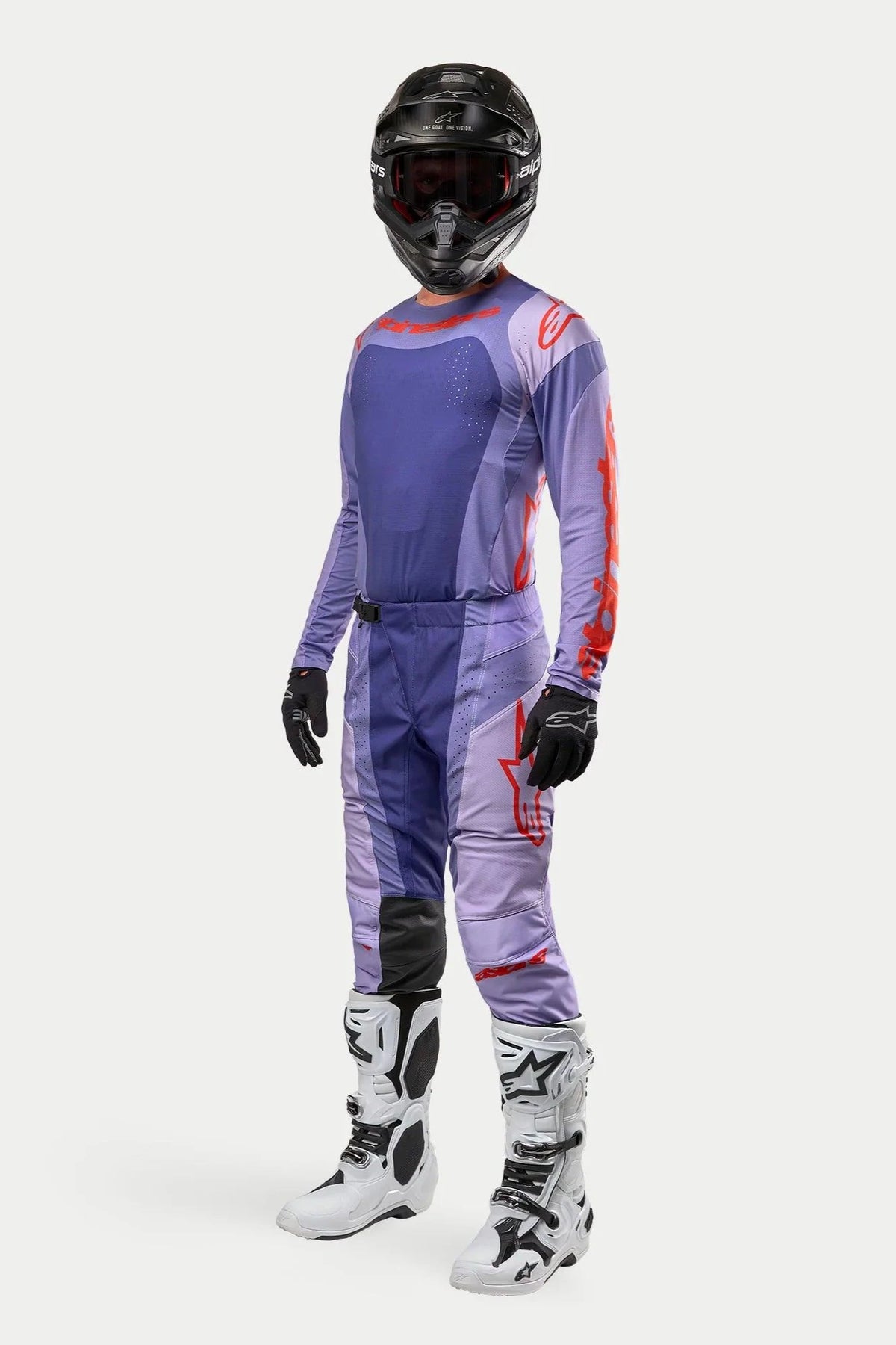 Pilote de motocross portant le maillot Alpinestars 2024 Techstar Ocuri en Purple Hot Orange, pantalon de course pourpre assorti avec des accents orange, casque noir, bottes blanches et noires, et gants noirs, tenue de compétition tout-terrain complète