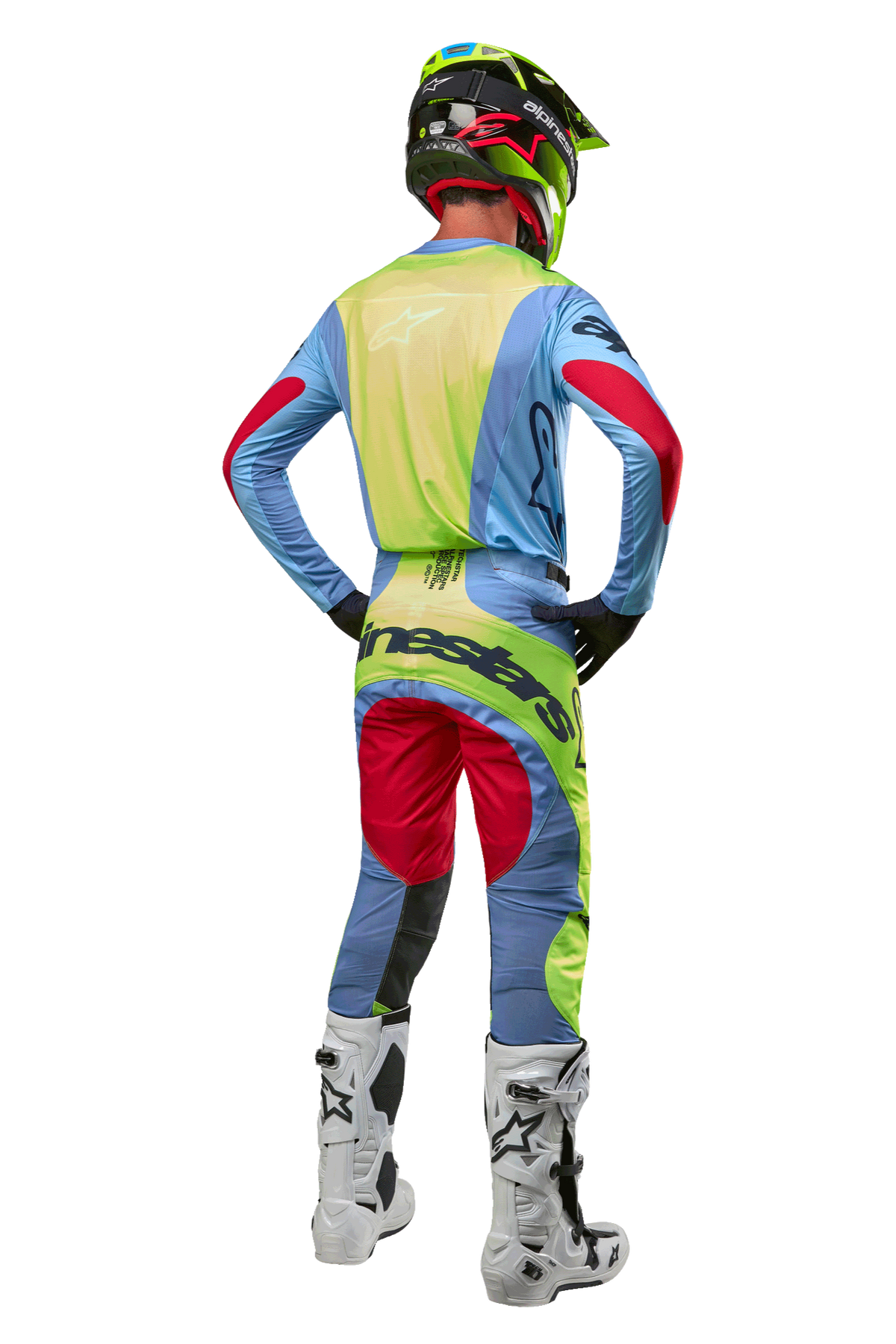 Pilote de motocross vu de dos portant le maillot Alpinestars Techstar Ocuri 2024, bleu clair avec accents jaune fluo et rouge berry, pantalon de course assorti, bottes blanches et casque fluo, équipement tout-terrain complet pour la compétition professionnelle