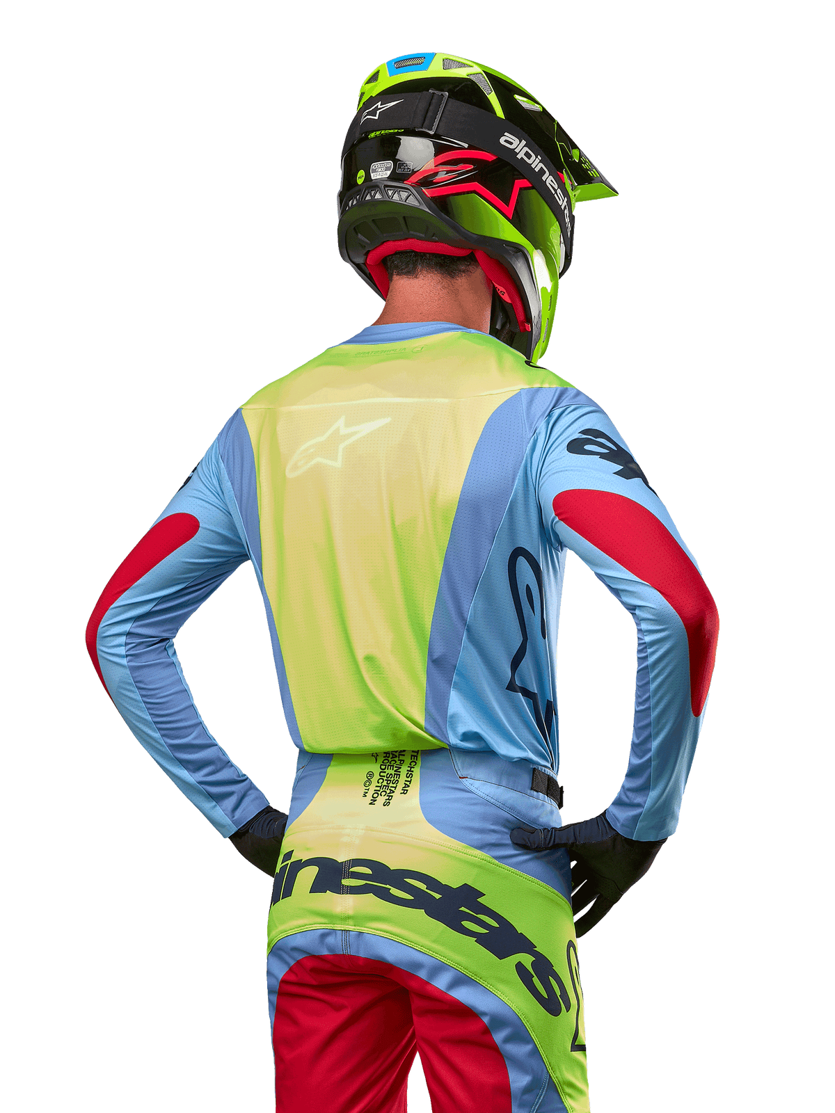 Pilote de motocross de dos portant le maillot Alpinestars Techstar Ocuri 2024, bleu clair avec dos jaune fluo et accents rouges sur les manches, pantalon de motocross assorti et casque jaune fluo, tenue coordonnée pour la course tout-terrain