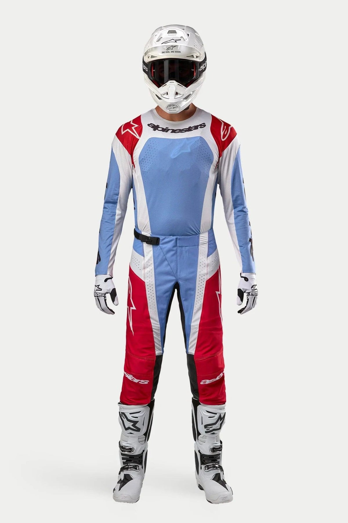 Pilote de motocross portant le maillot Alpinestars Techstar Ocuri 2024 en bleu clair, rouge Mars et blanc, pantalon de motocross assorti, casque blanc avec lunettes et bottes blanches, ensemble complet d'équipement de course tout-terrain professionnel