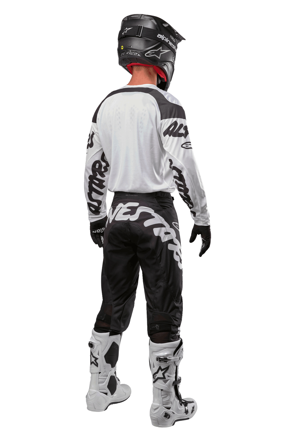 Maillot Alpinestars Racer Hana 2024, vue arrière d'un pilote de motocross, blanc et noir, maillot blanc avec marquage graphique noir sur les manches, associé à un pantalon noir avec lettrage Alpinestars blanc sur l'assise, casque noir et bottes blanches et noires, équipement de course tout-terrain coordonné