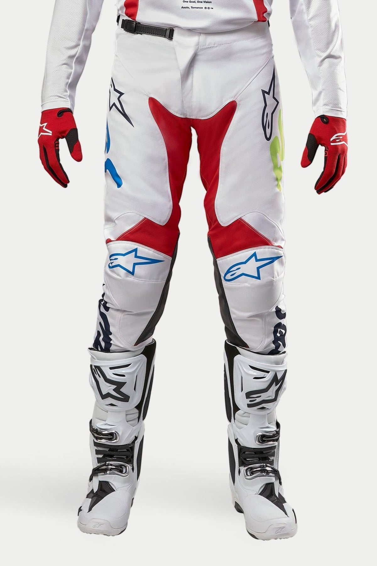 Pantalon Alpinestars Racer Hana 2024, pantalon de motocross, blanc multicolore avec des accents rouges, bleus et vert citron, porté avec des bottes blanches et noires et des gants rouges, avec logos Alpinestars sur les genoux et conception technique durable pour la course tout-terrain