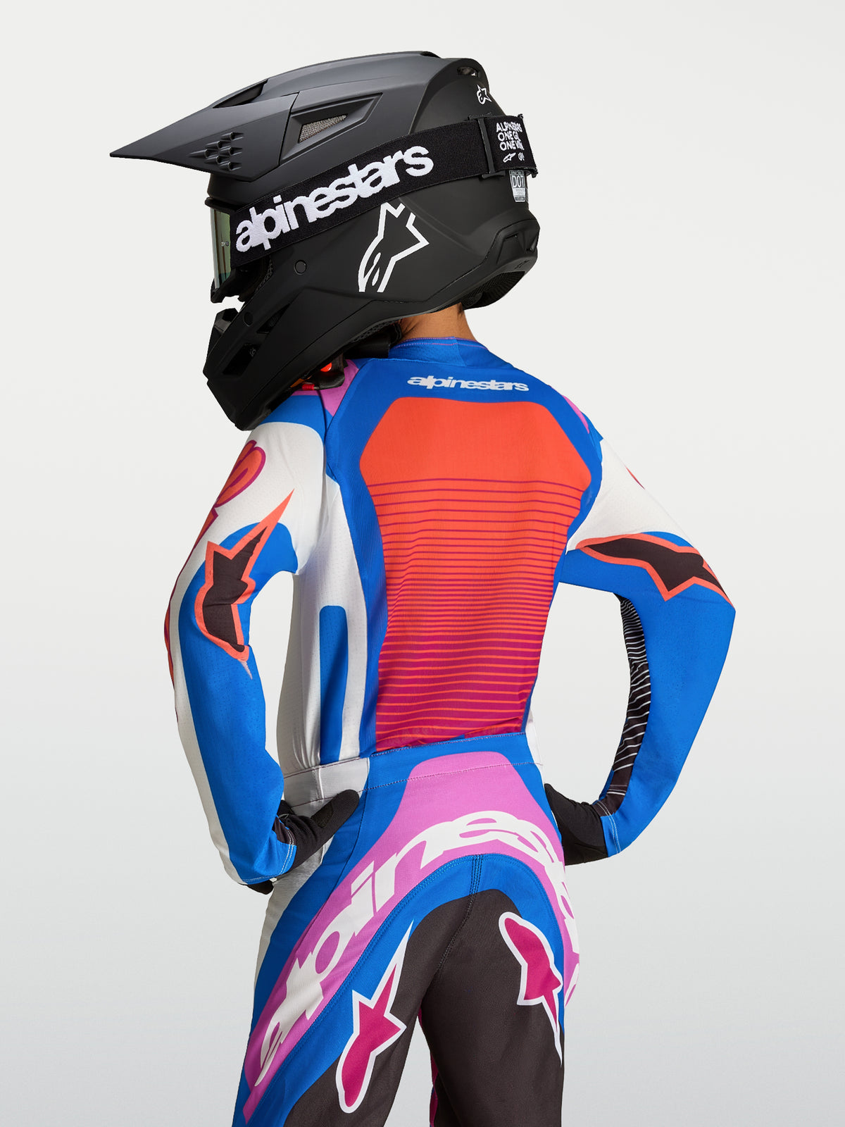 Alpinestars Maillot Supertech Maven Junior, maillot de motocross pour enfant, bleu et orange corail, coupe athlétique en maille extensible aérée, vue de dos sur un pilote