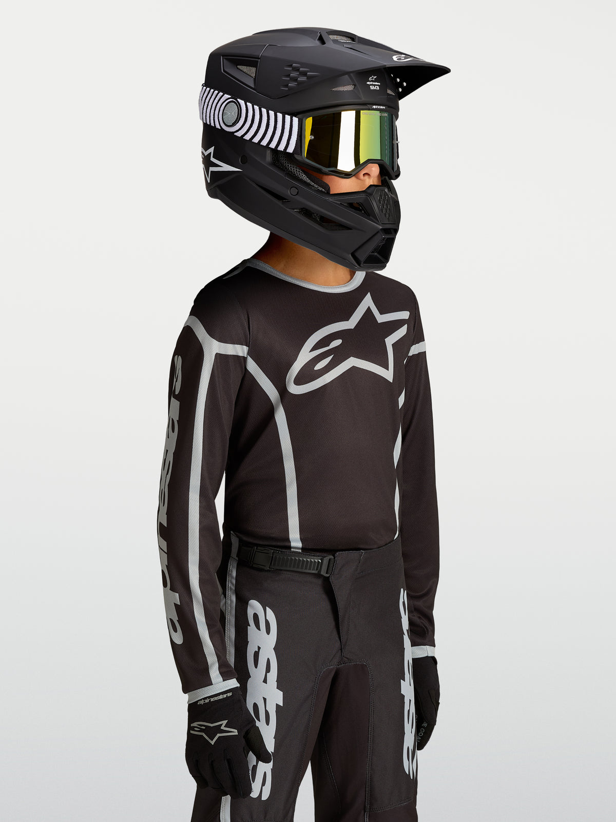 Maillot Alpinestars Fluid Apex V2 Junior, haut de motocross pour enfant, noir et argenté, textile respirant avec logo Astars, porté par un jeune pilote