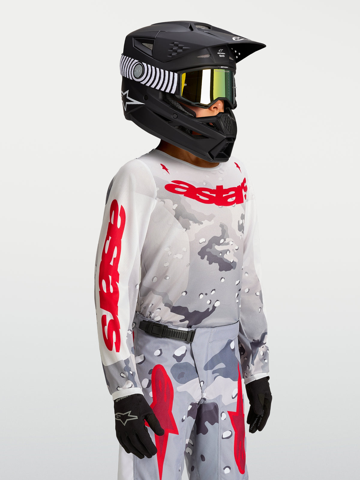 Maillot Alpinestars Fluid Lone Junior 2027, maillot de motocross gris camouflage et rouge, porté avec un casque.