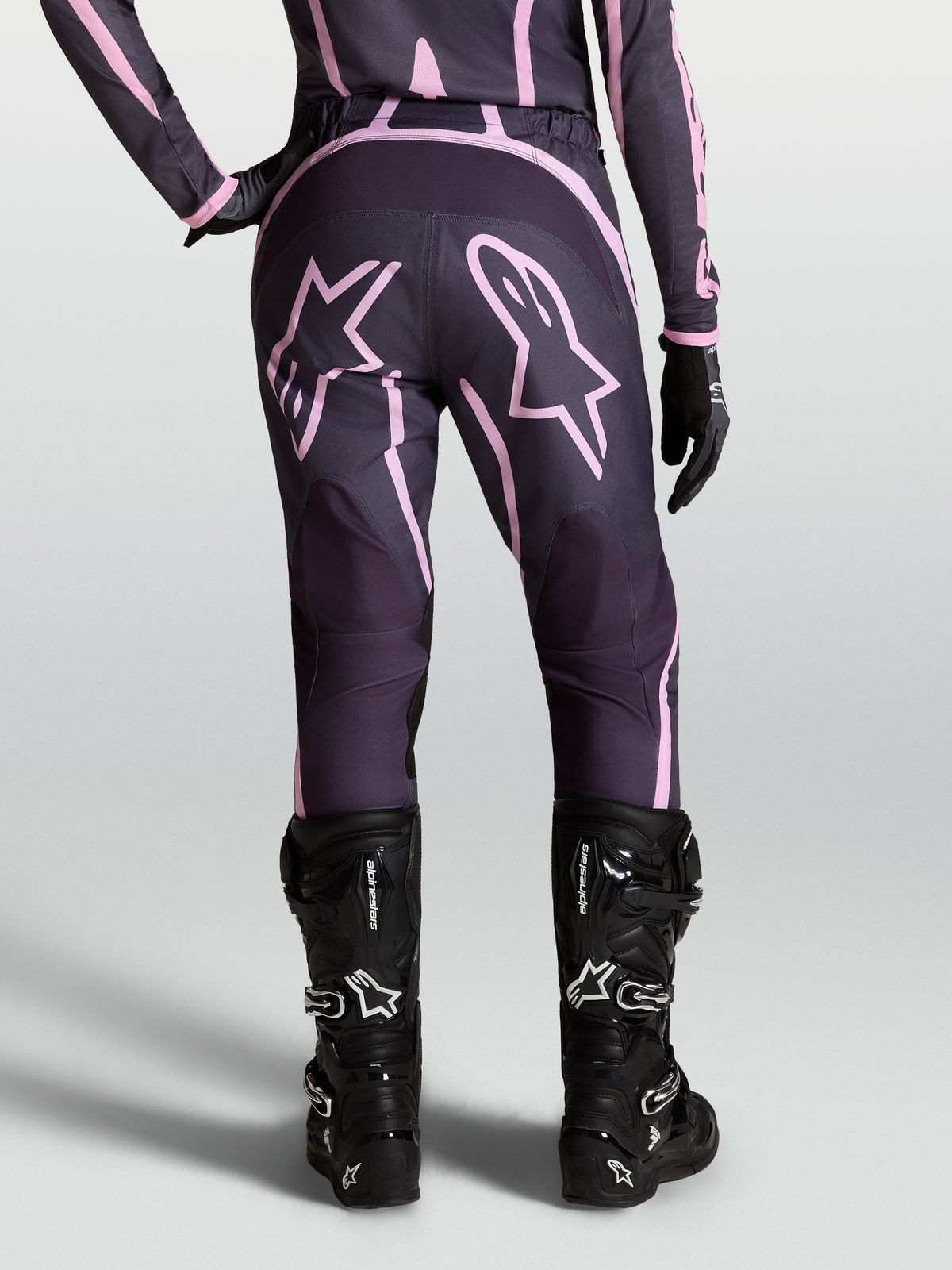 Alpinestars Stella Fluid Apex V2, pantalons de motocross pour femme, gris et rose, vue arrière avec graphismes d'étoiles et bottes noires, équipement de performance tout-terrain