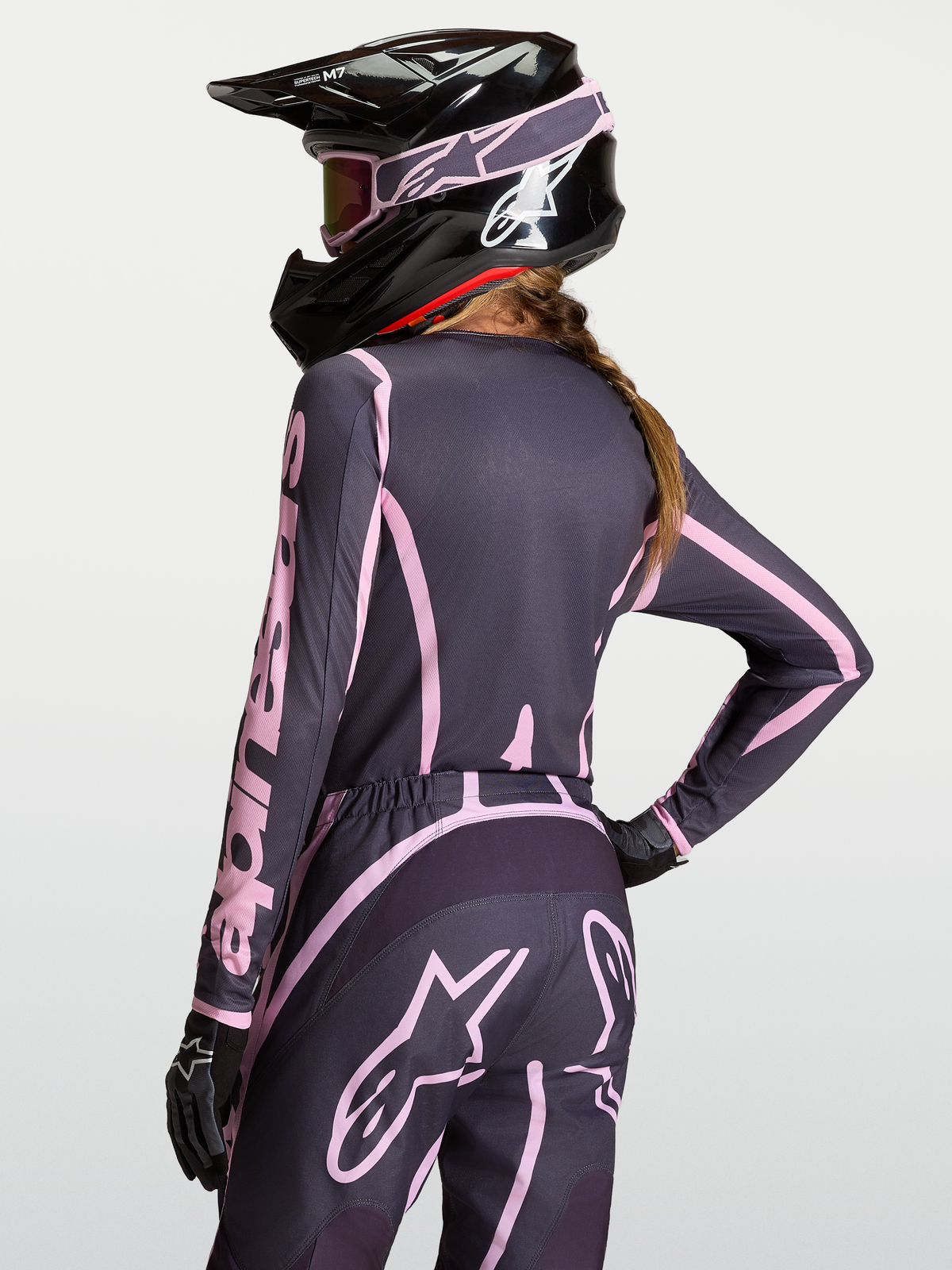 Maillot Stella Fluid Apex V2 d'Alpinestars, équipement de motocross pour femme gris et rose vieilli, porté avec un pantalon assorti et un casque noir.