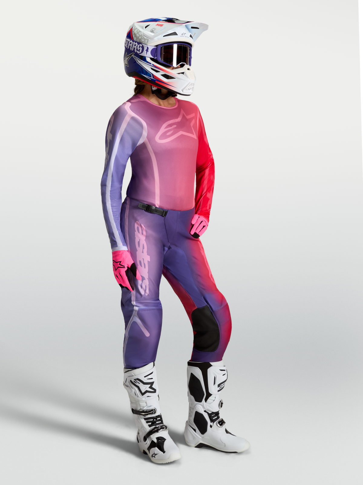 Maillot Alpinestars Stella Fluid Kepler pour femme, violet et rouge, porté avec un pantalon assorti et des bottes blanches.